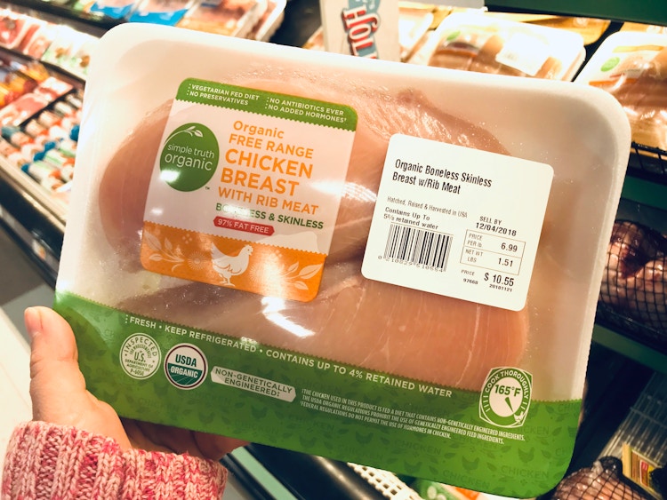 A person holding a package of chicken breasts.