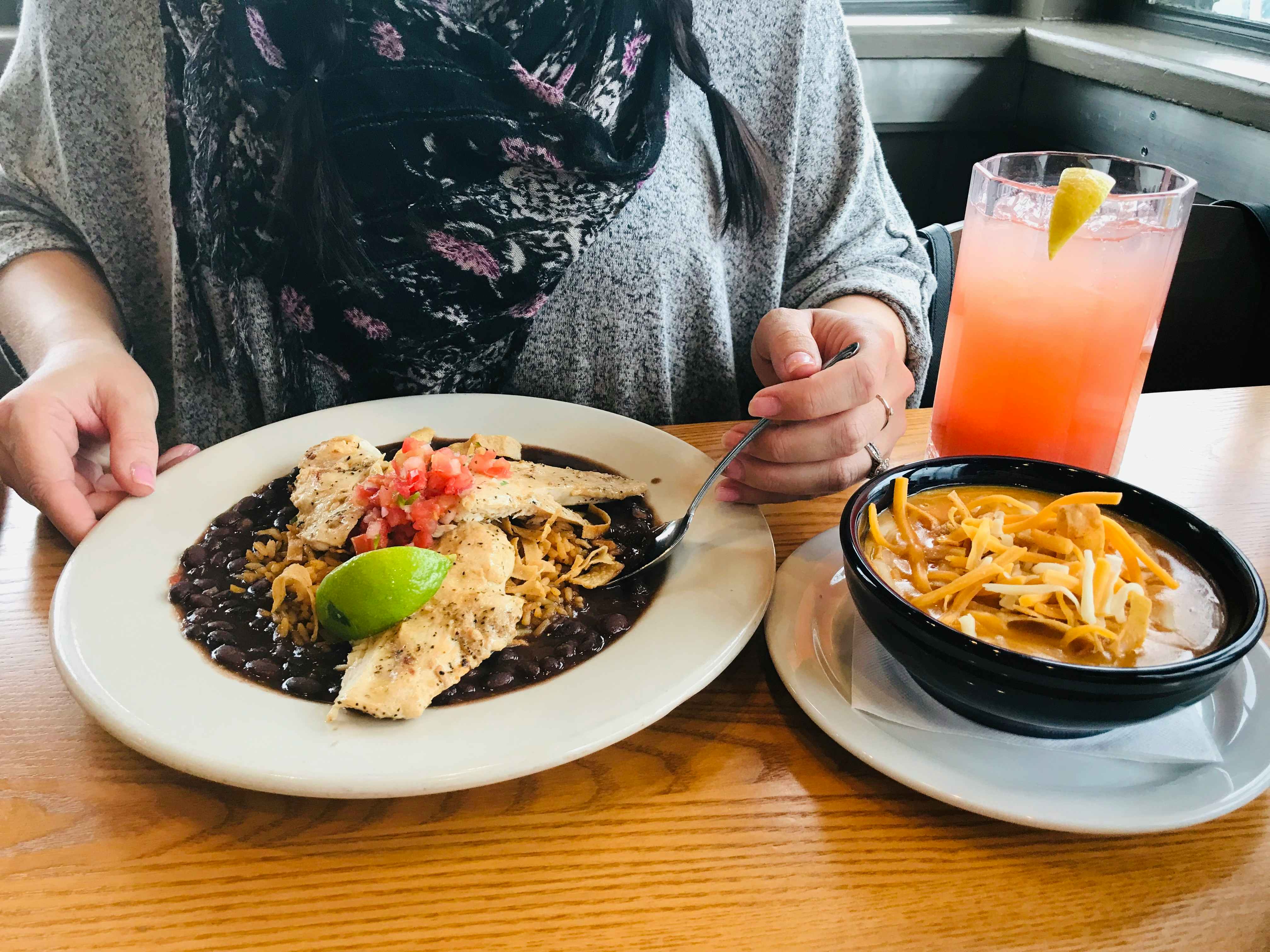 A person sitting in a Chili's booth with a meal and lemonade on the table in front of her.