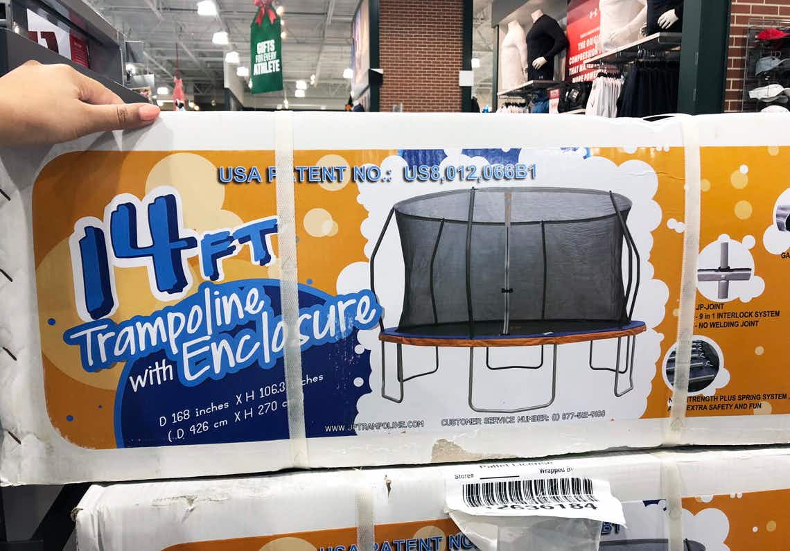 A person's hand grabbing the box for a 14 ft trampoline stocked at Dick's Sporting Goods.