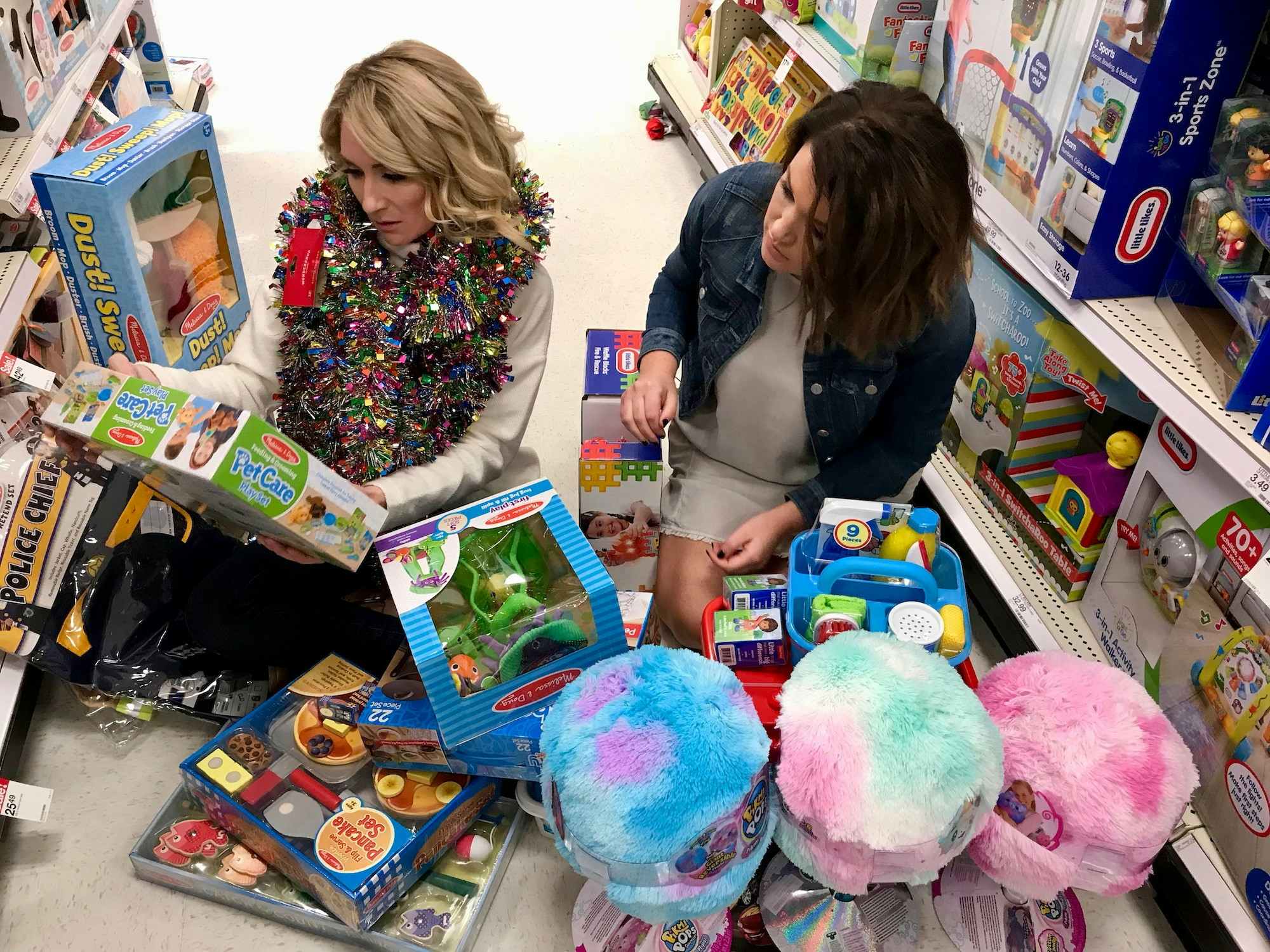 Two women sitting in the middle of a toy aisle surrounded by toys on Black Friday.