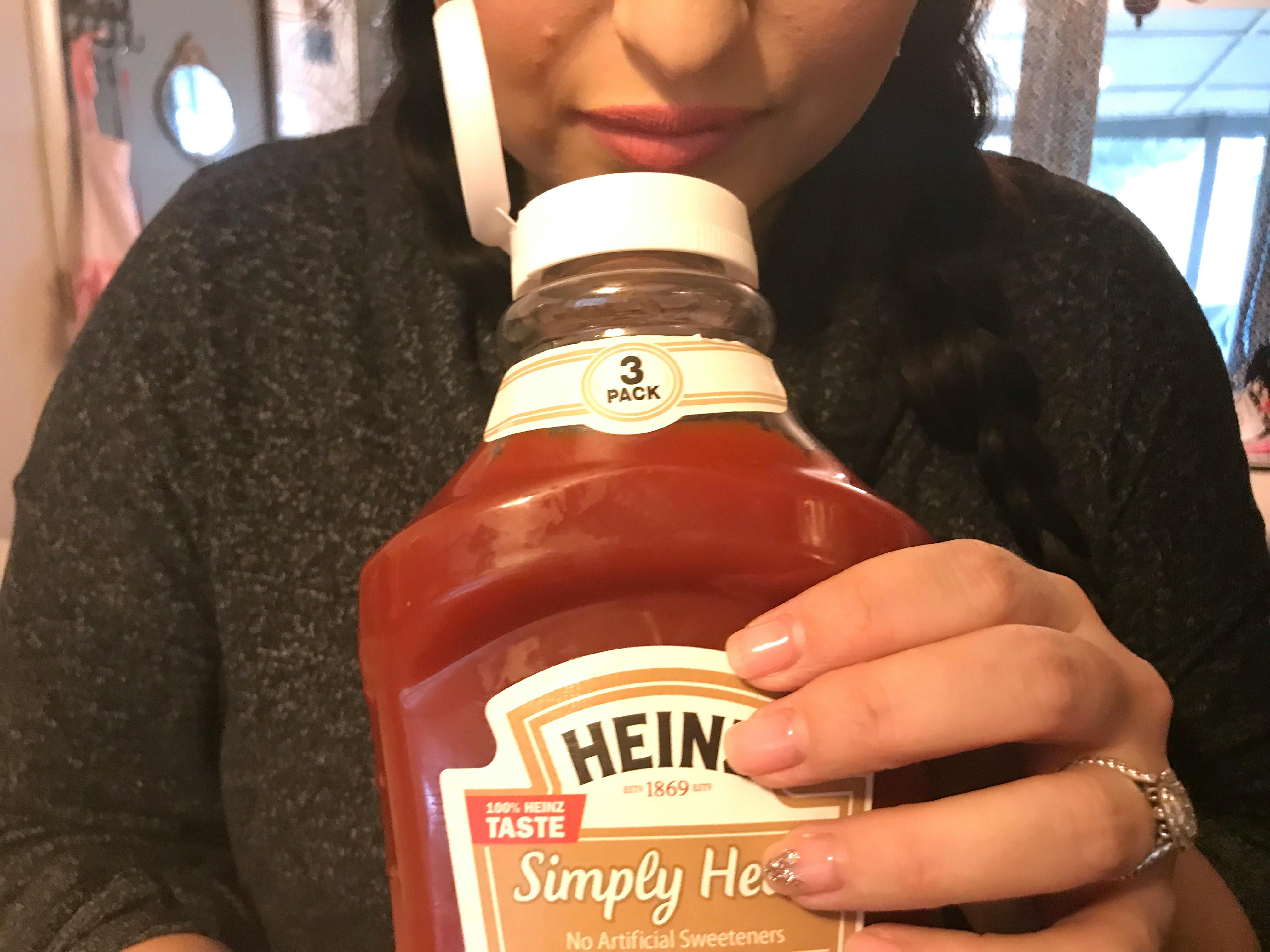 A person smelling a bottle of Heinz ketchup.