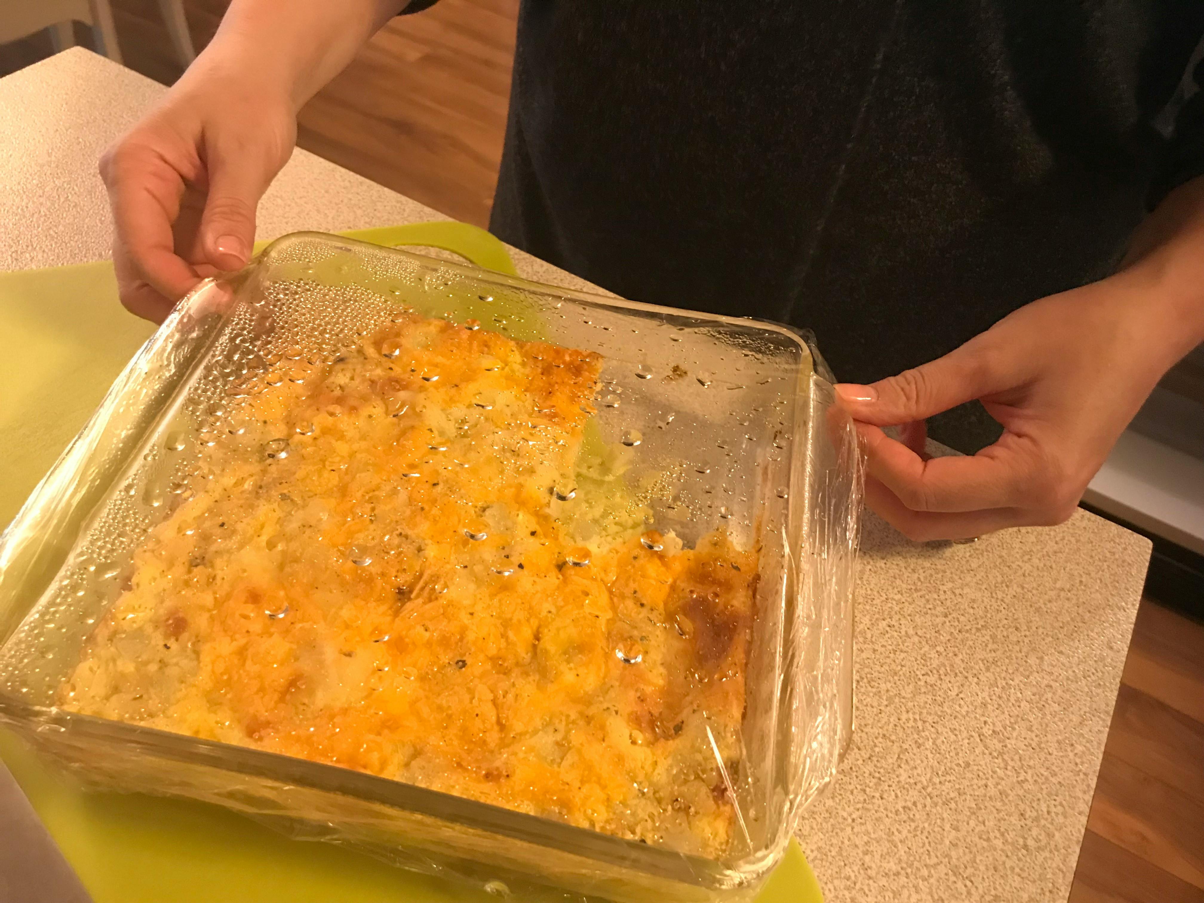 A person putting saran wrap over a dish of leftover food.