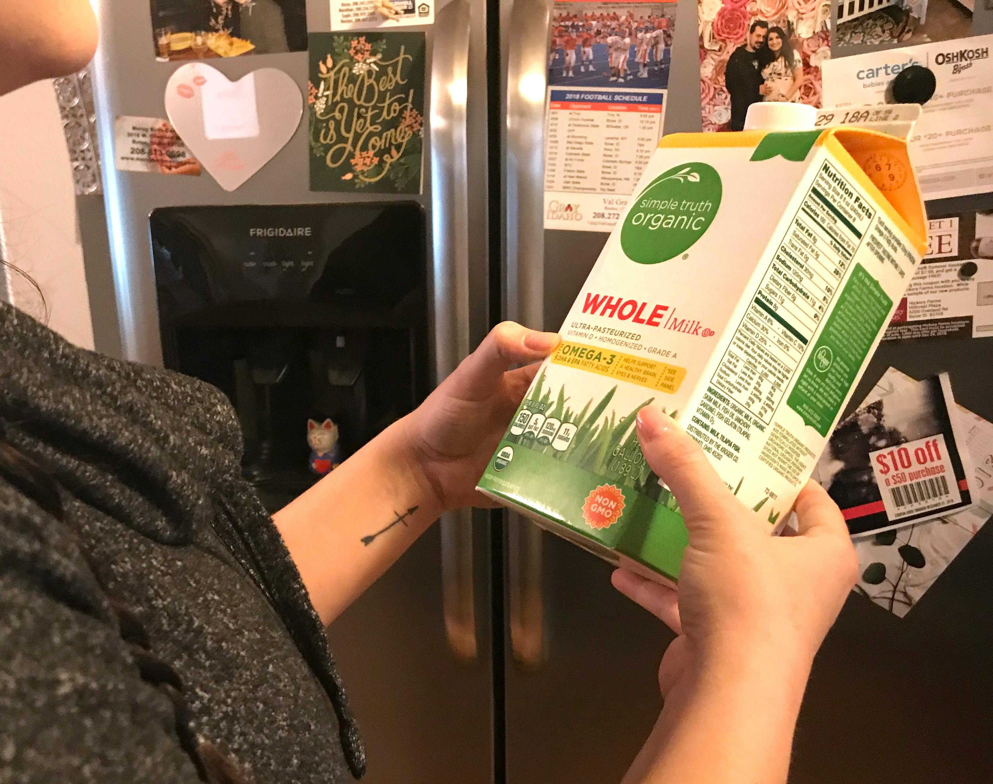 A person holding a carton of milk in front of an open refrigerator.