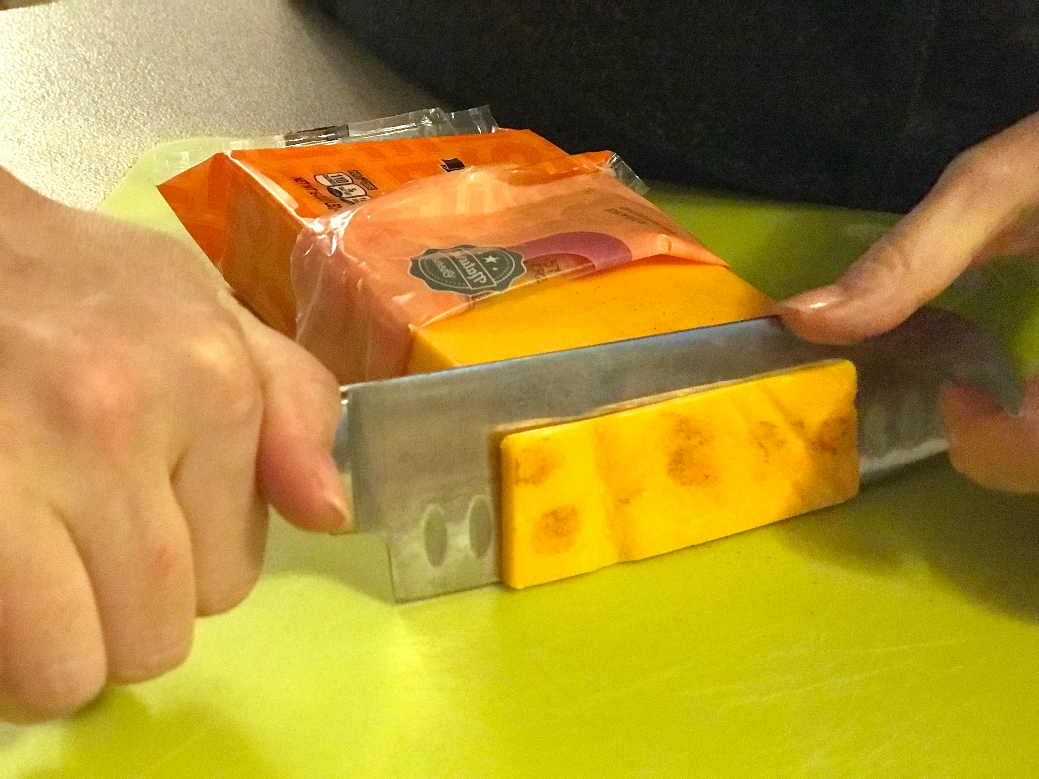 A person cutting of mold from a block of cheese.