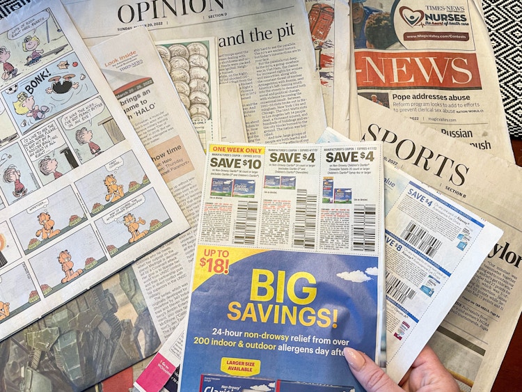 a person pulling coupon inset out of newspaper