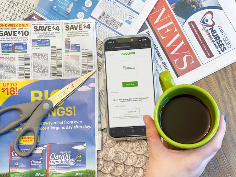 hand holding a cup of coffee above a phone on and newspaper