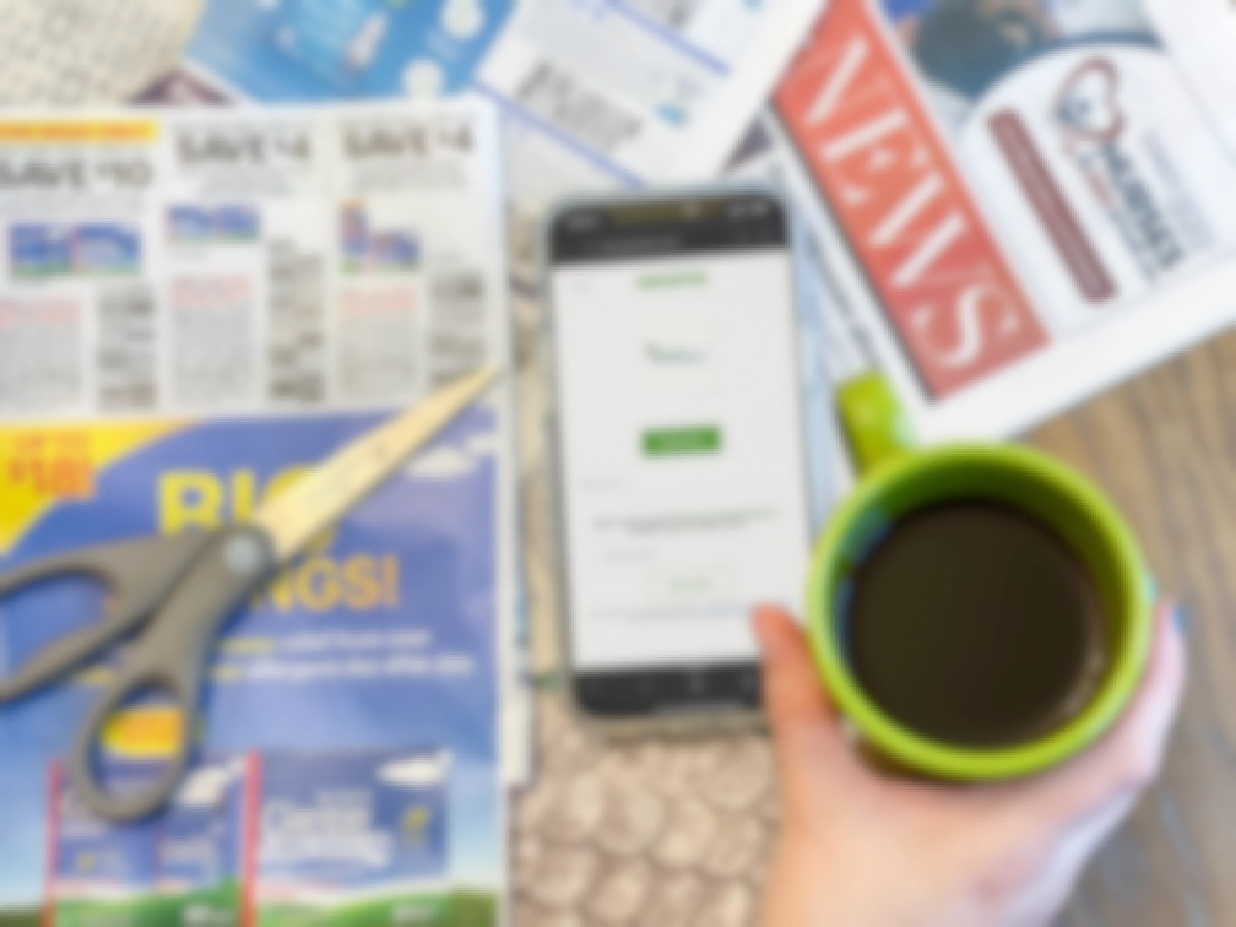 hand holding a cup of coffee above a phone on and newspaper