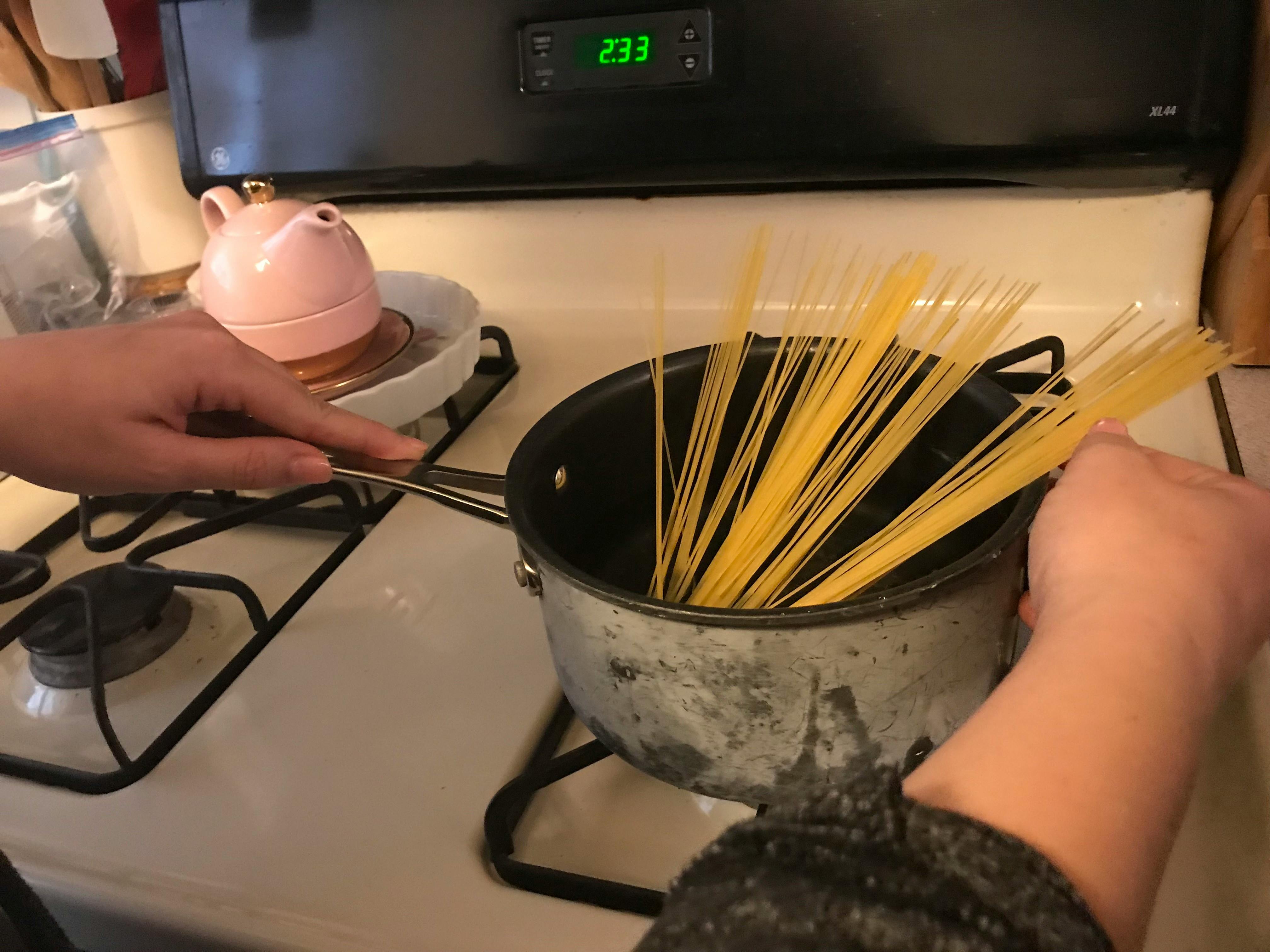 A person holding a pan of pasta on a stove.