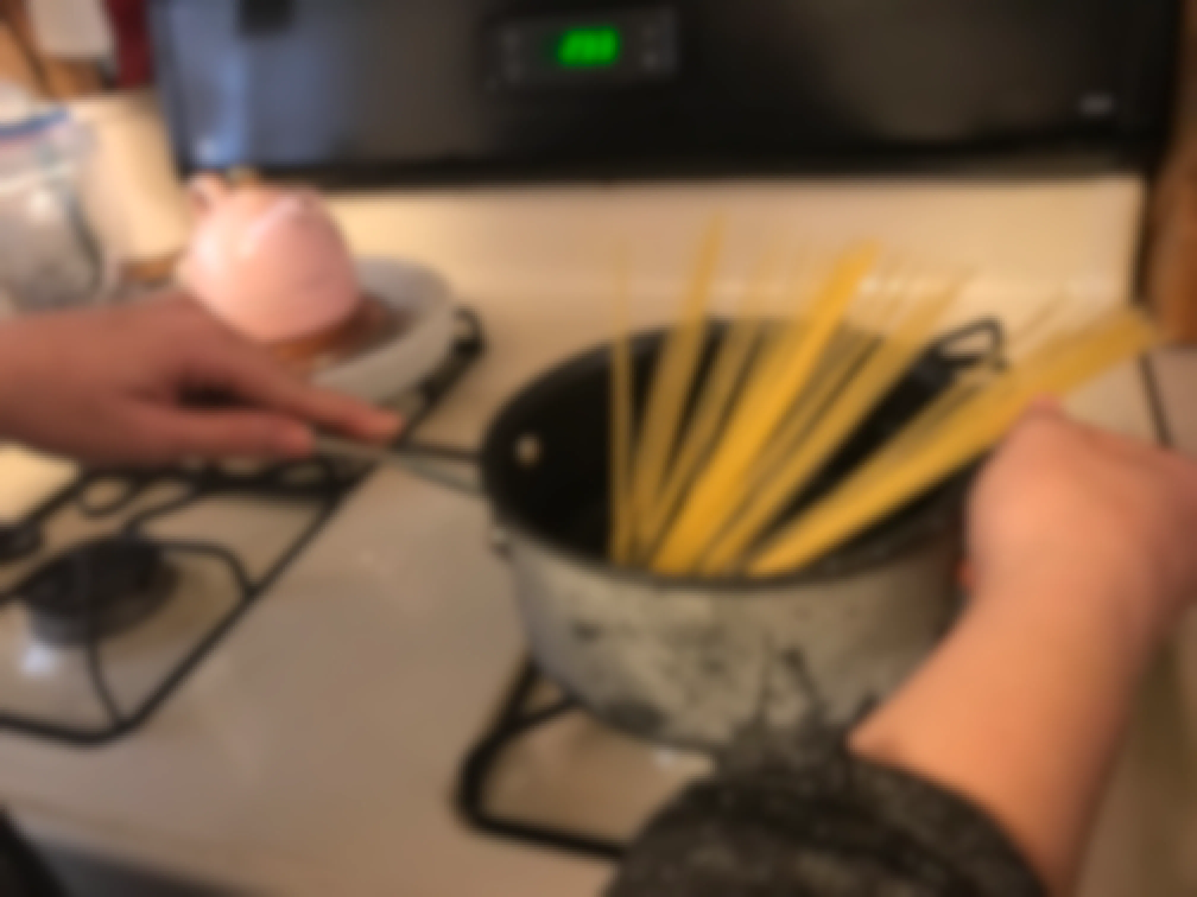 A person holding a pan of pasta on a stove.