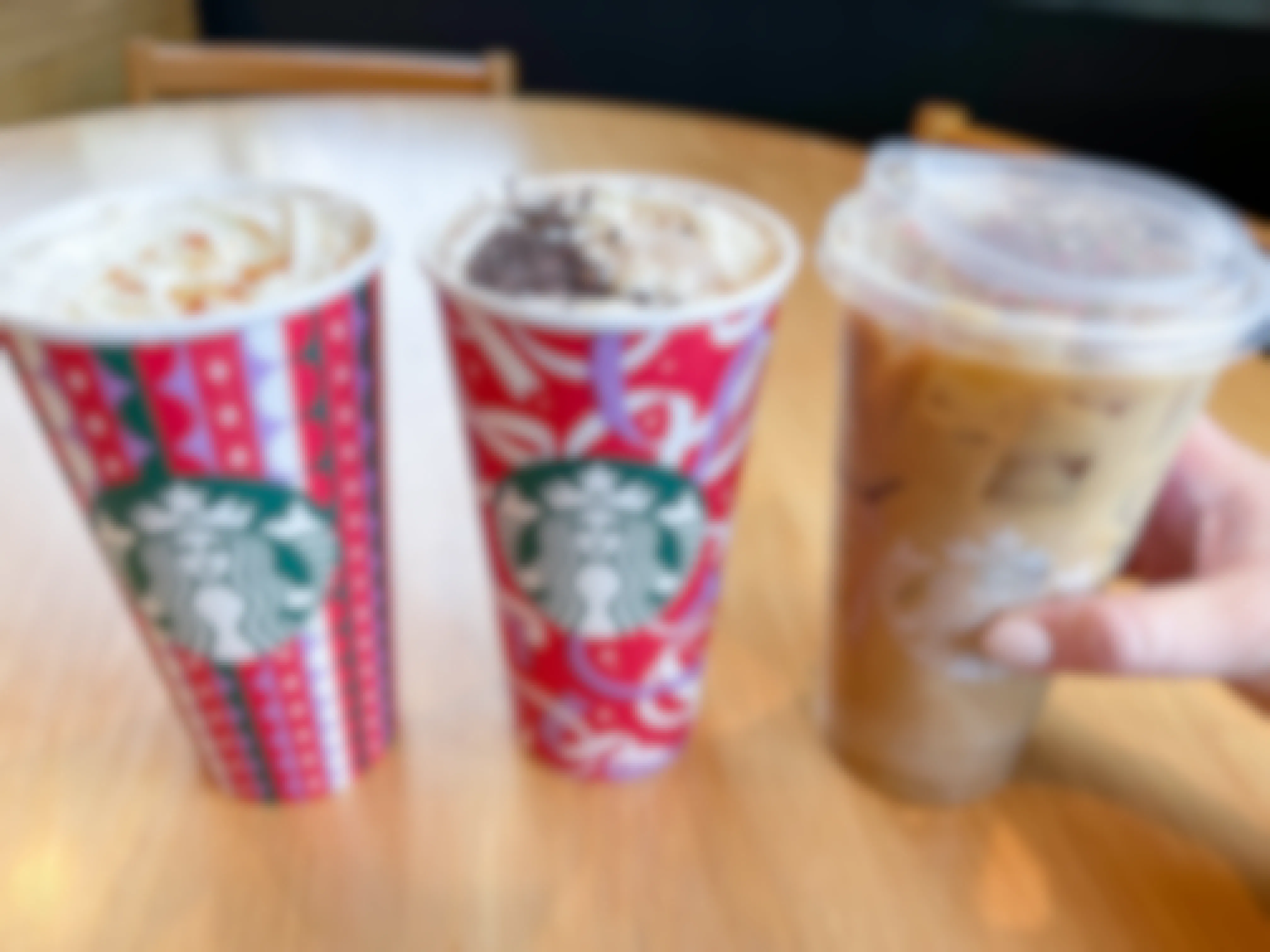Three Starbucks holiday drinks on a table with one being grabbed 
