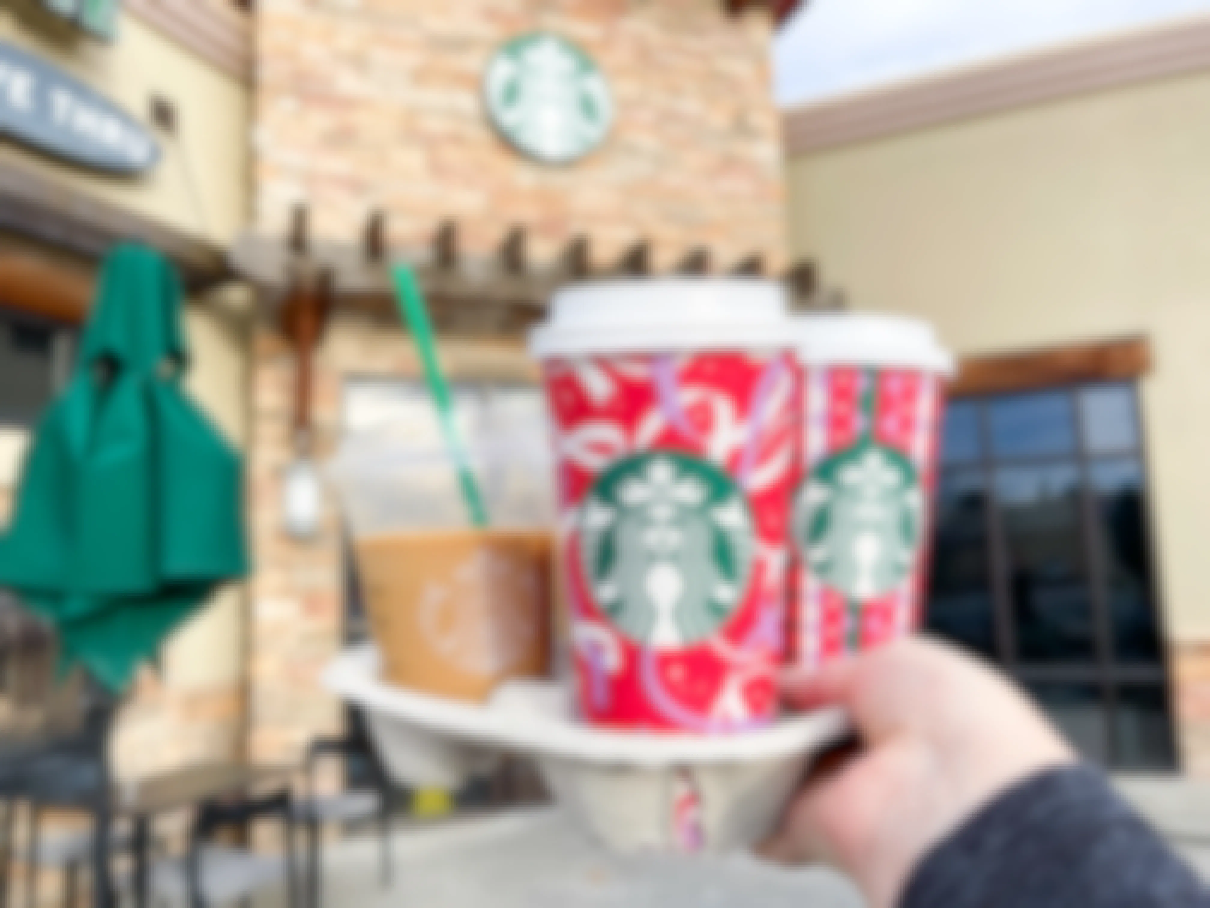 A person holding up a drink carrier holding some holiday drinks in front of a Starbucks. You can get these drinks on Christmas because Starbucks is open on Christmas.