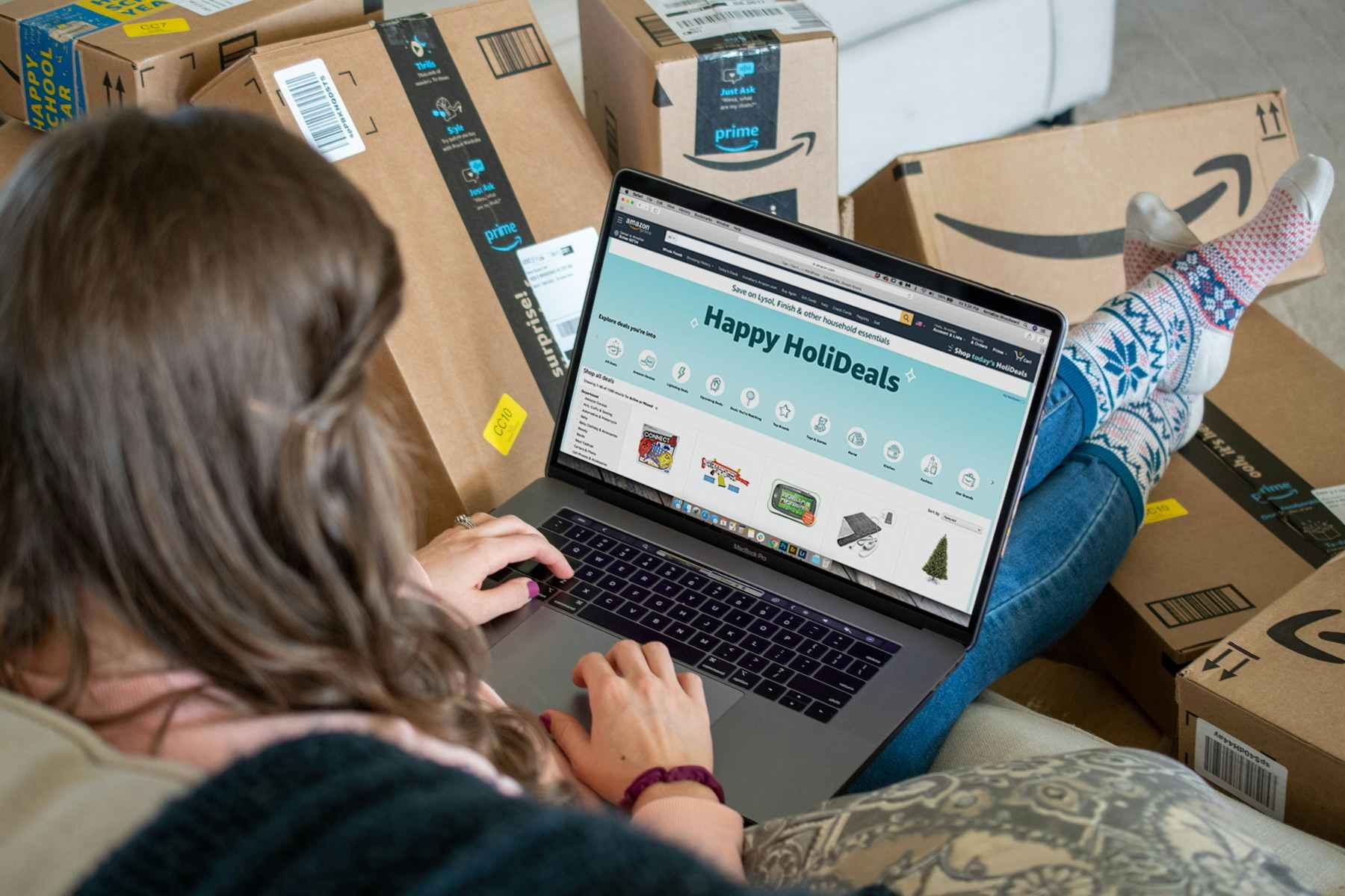 A woman shopping on Amazon on a laptop surrounded by Amazon boxes