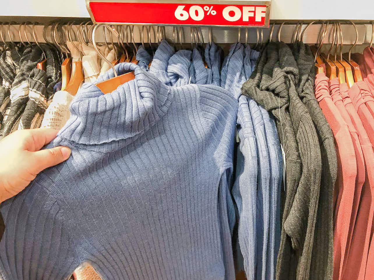 A person taking a turtleneck sweater from a rack of them marked as 60% off at American Eagle.