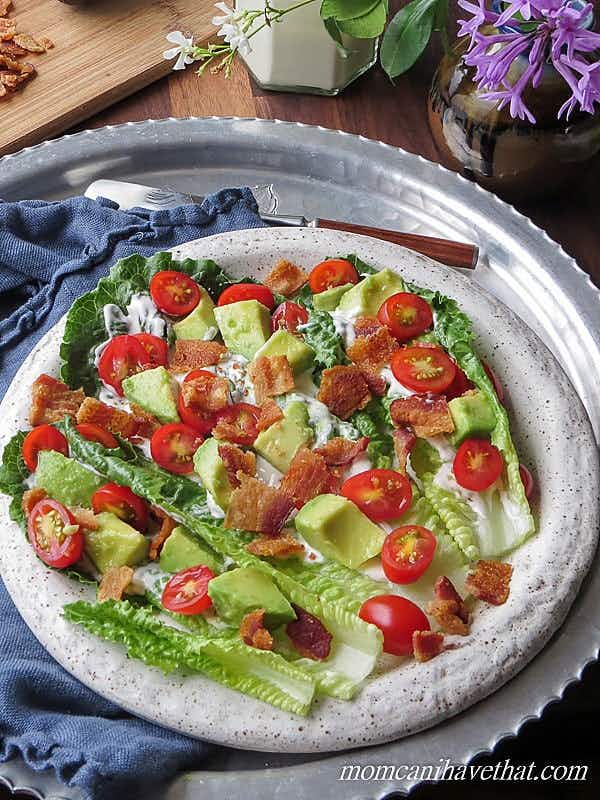 A salad with bacon, tomato, avocado and dressing on a plate
