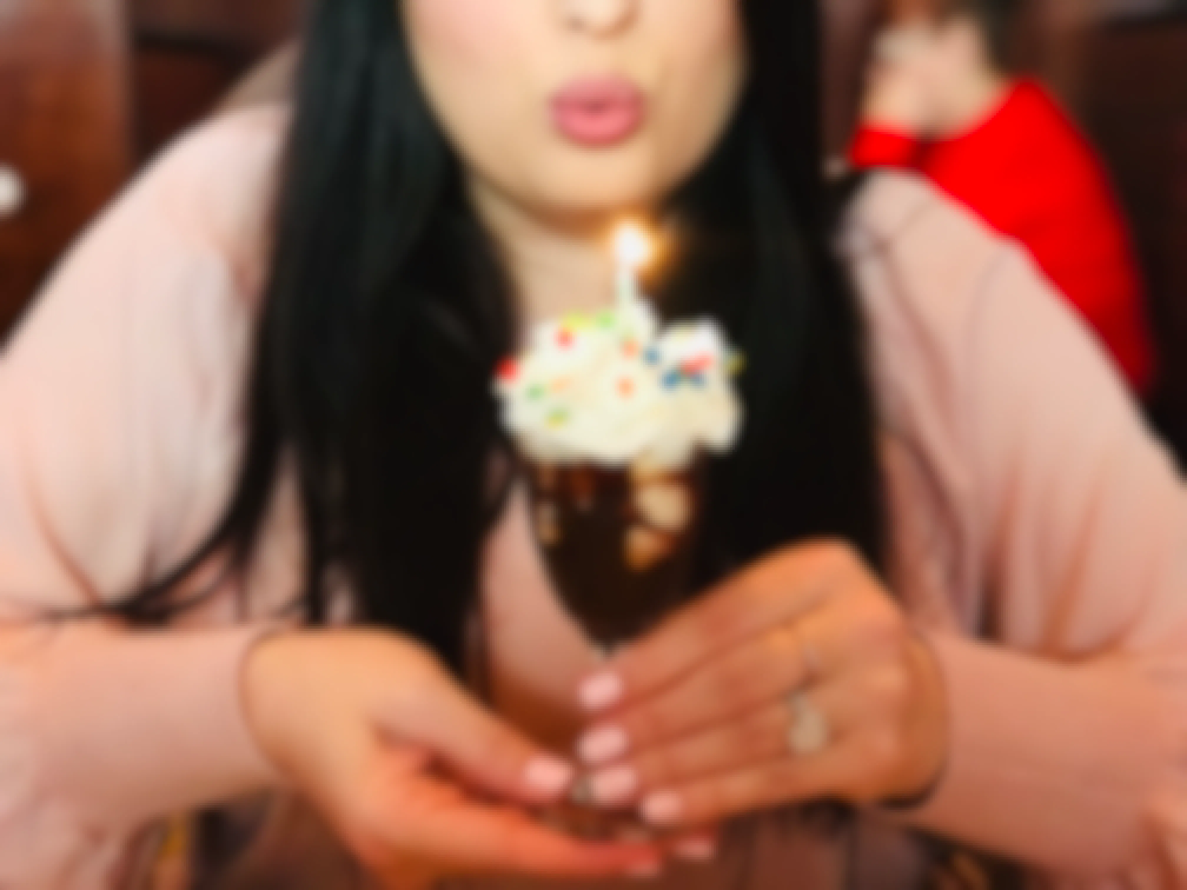 A person about to blow out a lit candle on top of a small sundae.