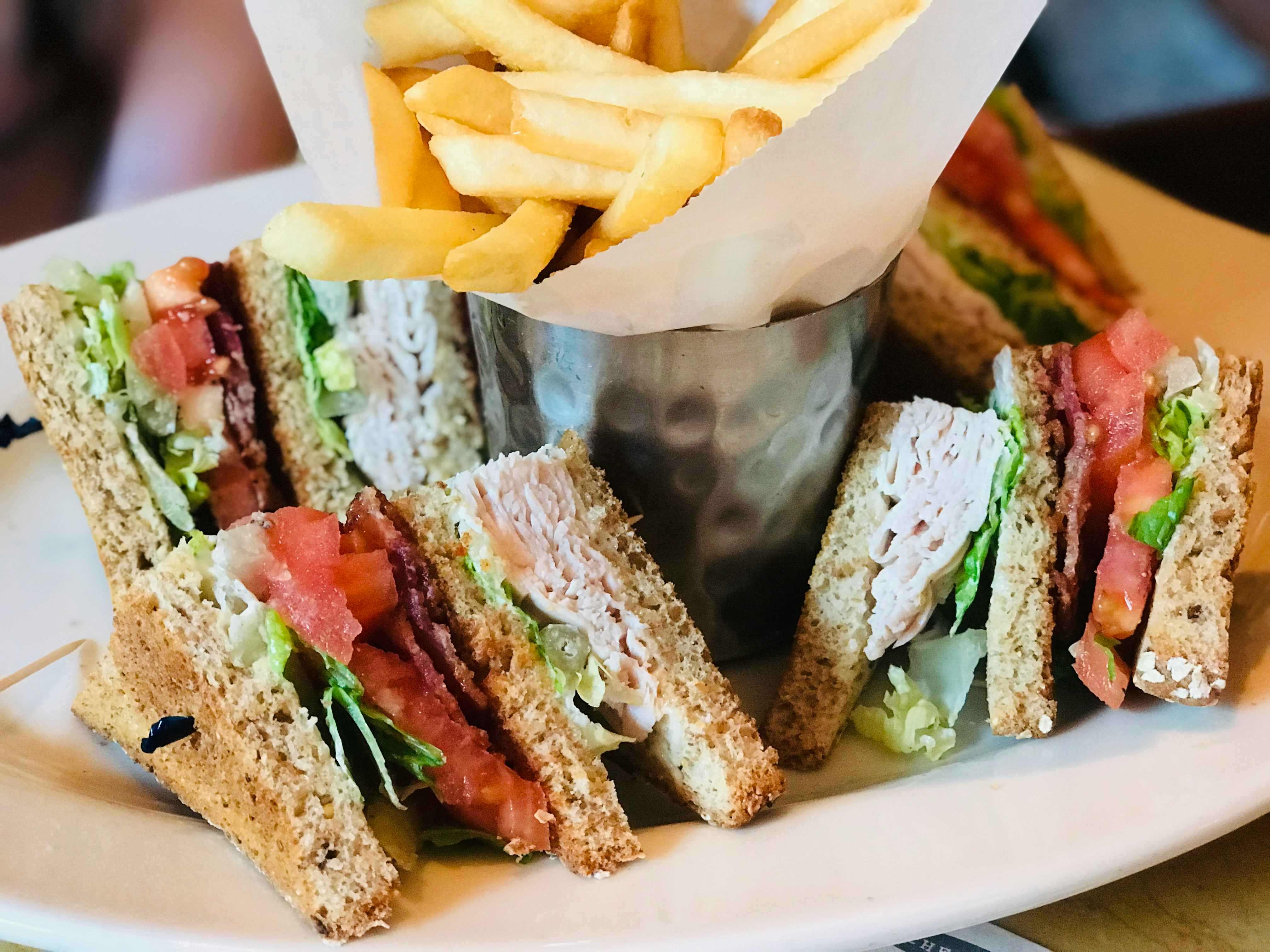 A plate of small sandwiches surrounding a metal cup filled with french fries.