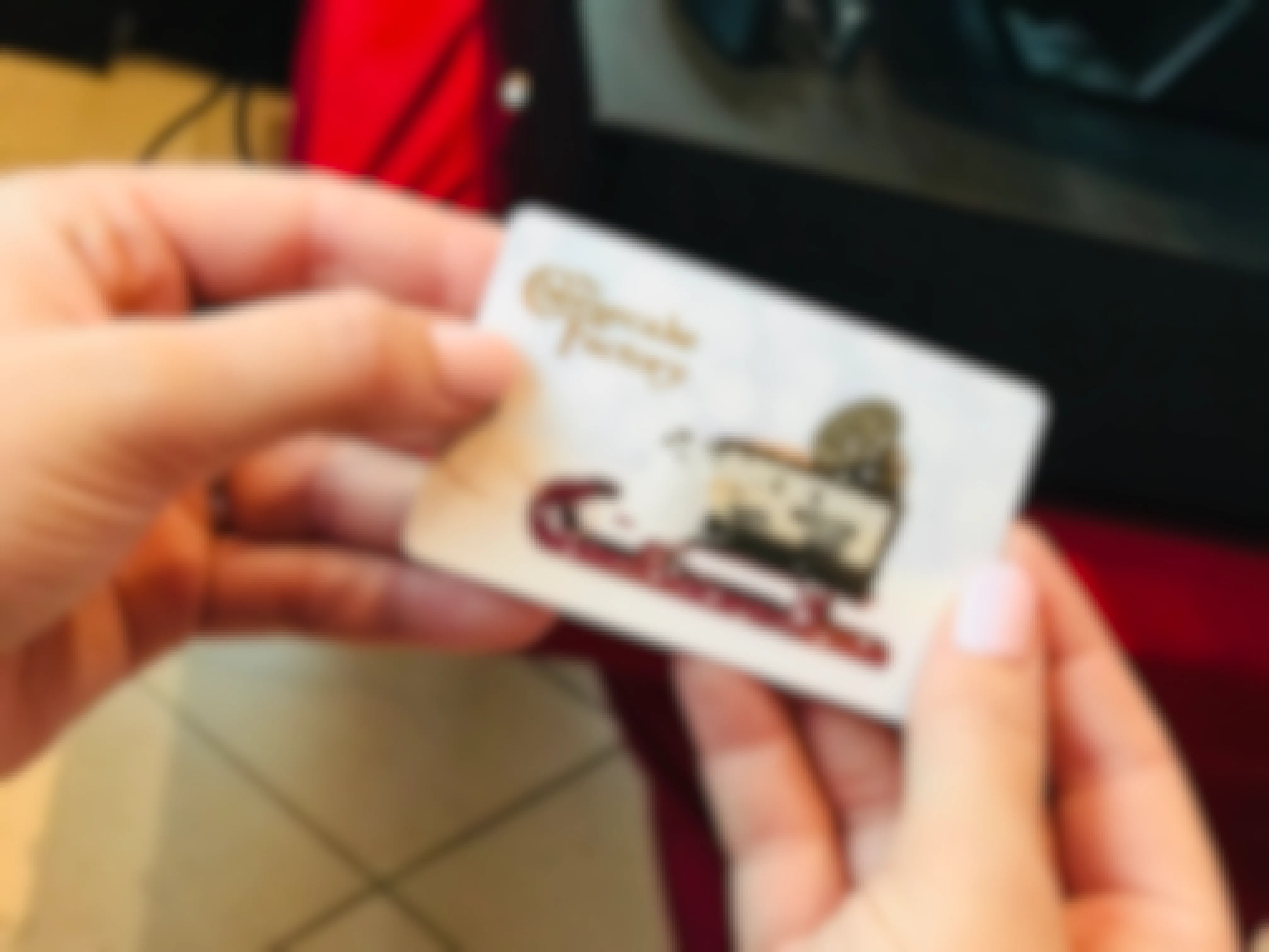 A person's hands holding a gift card for The Cheesecake Factory.