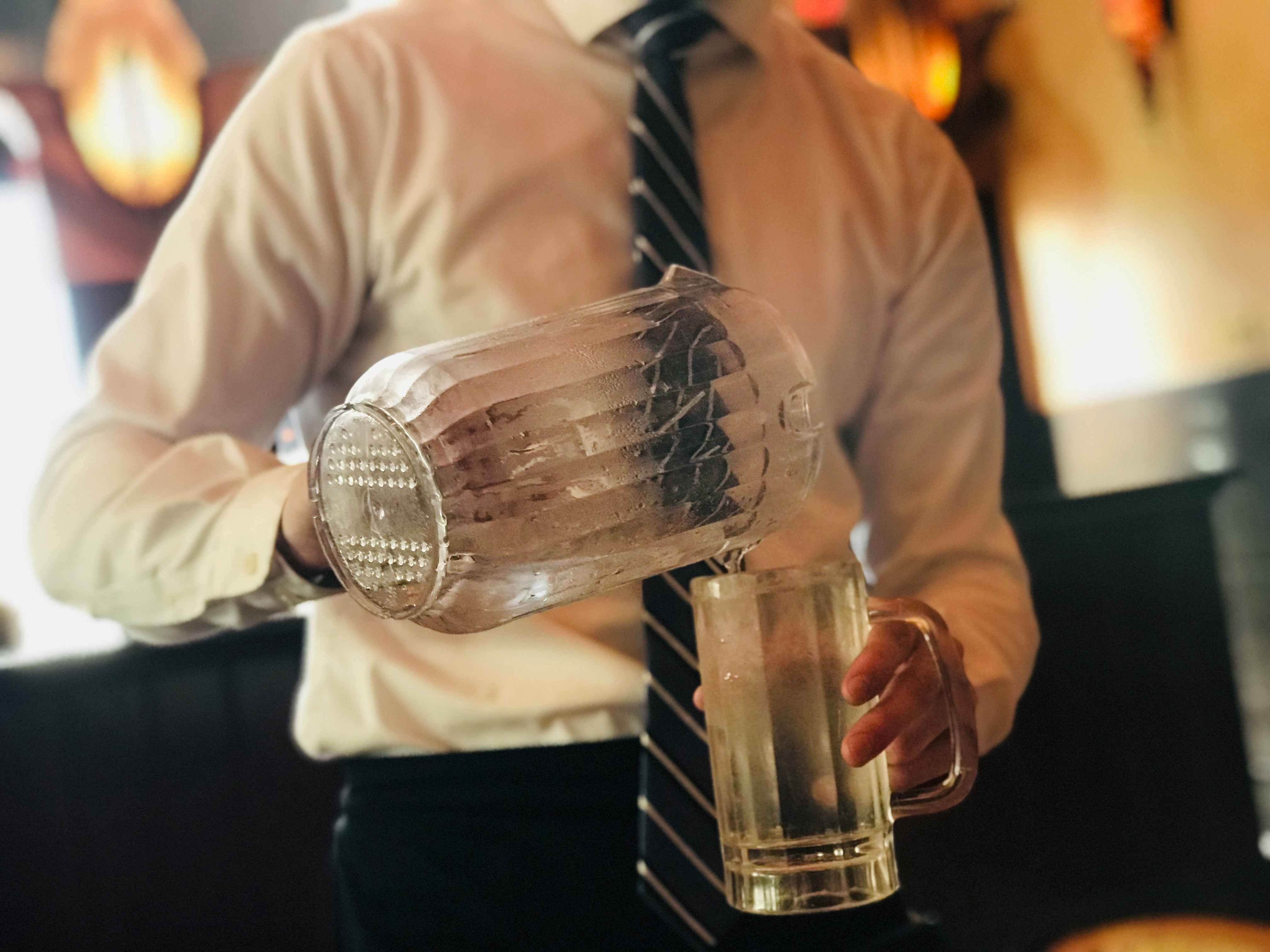 A server pouring water from a pitcher into a glass at a table in The Cheesecake Factory.