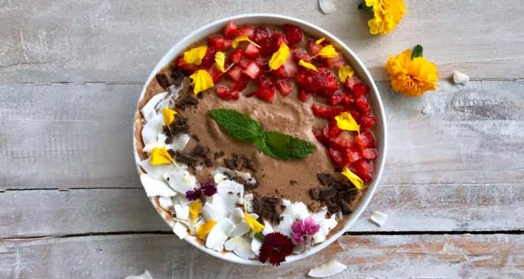 A chocolate smoothie bowl with coconut, strawberries, mint