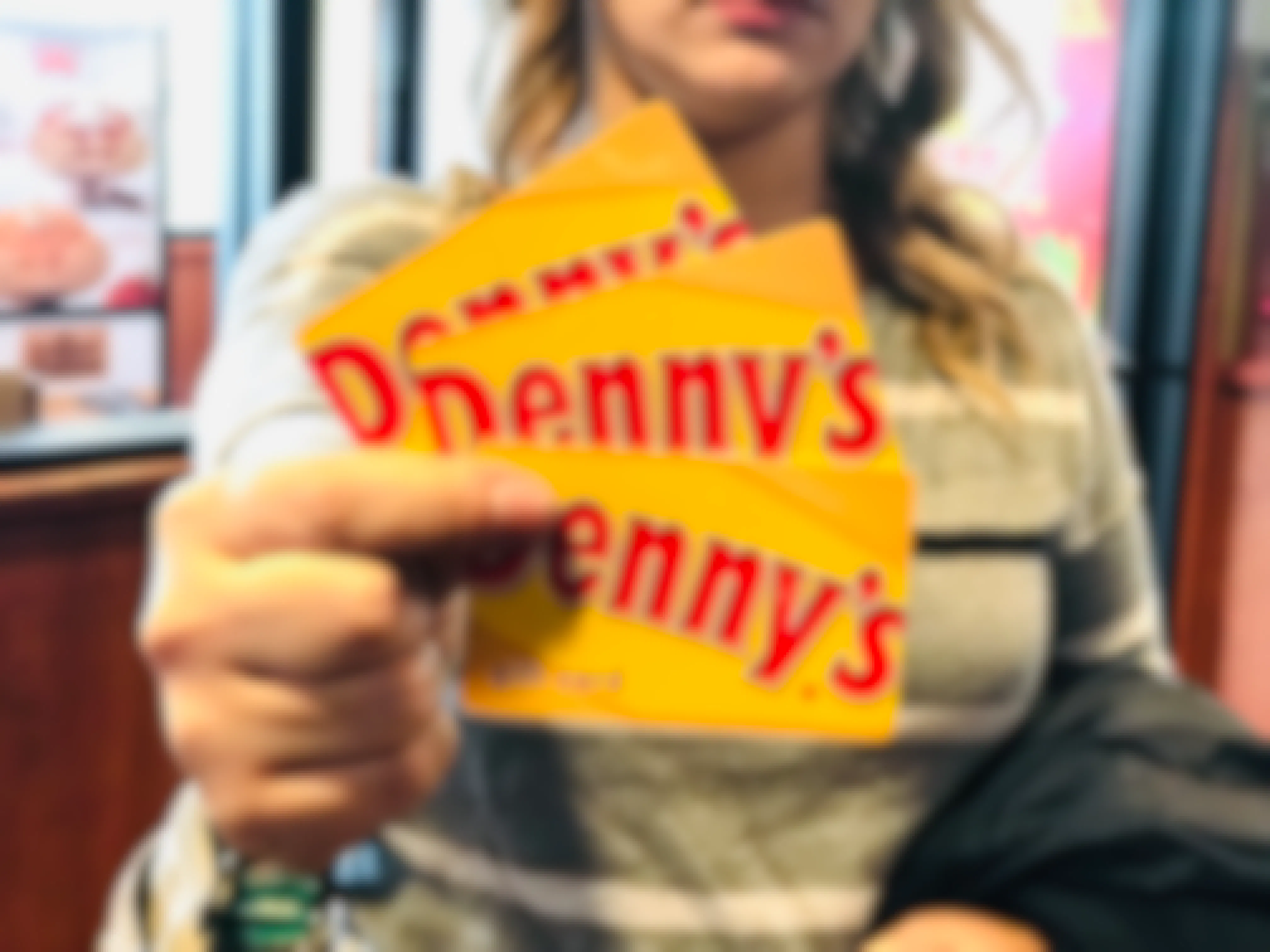A person standing inside Denny's and holding up three Denny's gift cards to the camera.