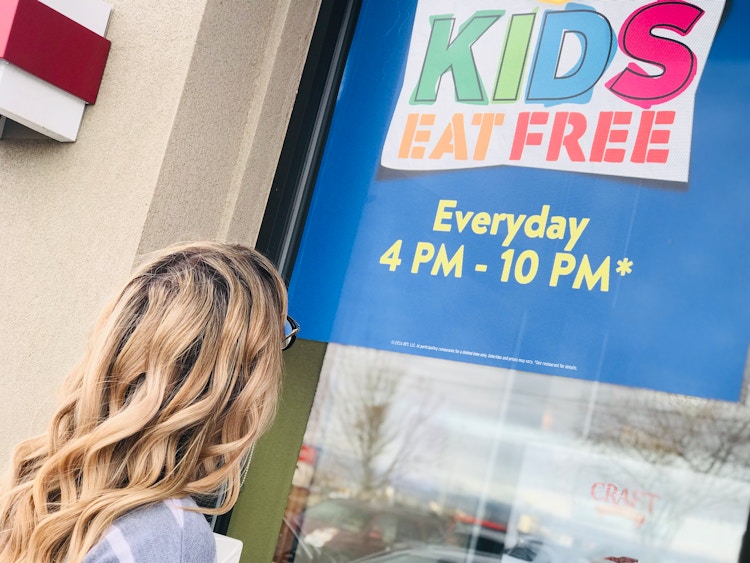 A person facing away from the camera and looking up at a sign in the window at Denny's which reads, 