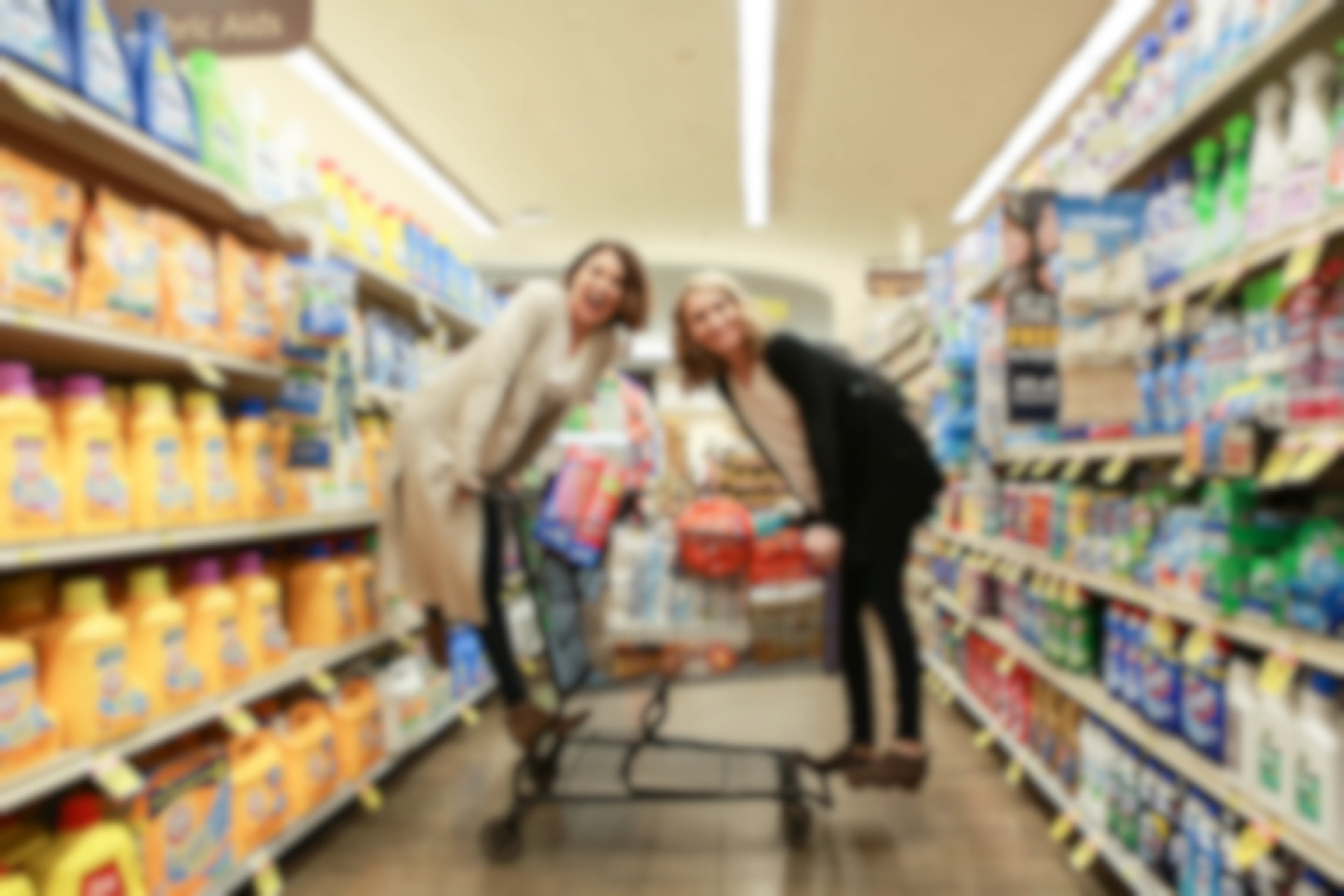 Two women balancing on a full shopping cart of groceries in the middle of a Kroger store aisle