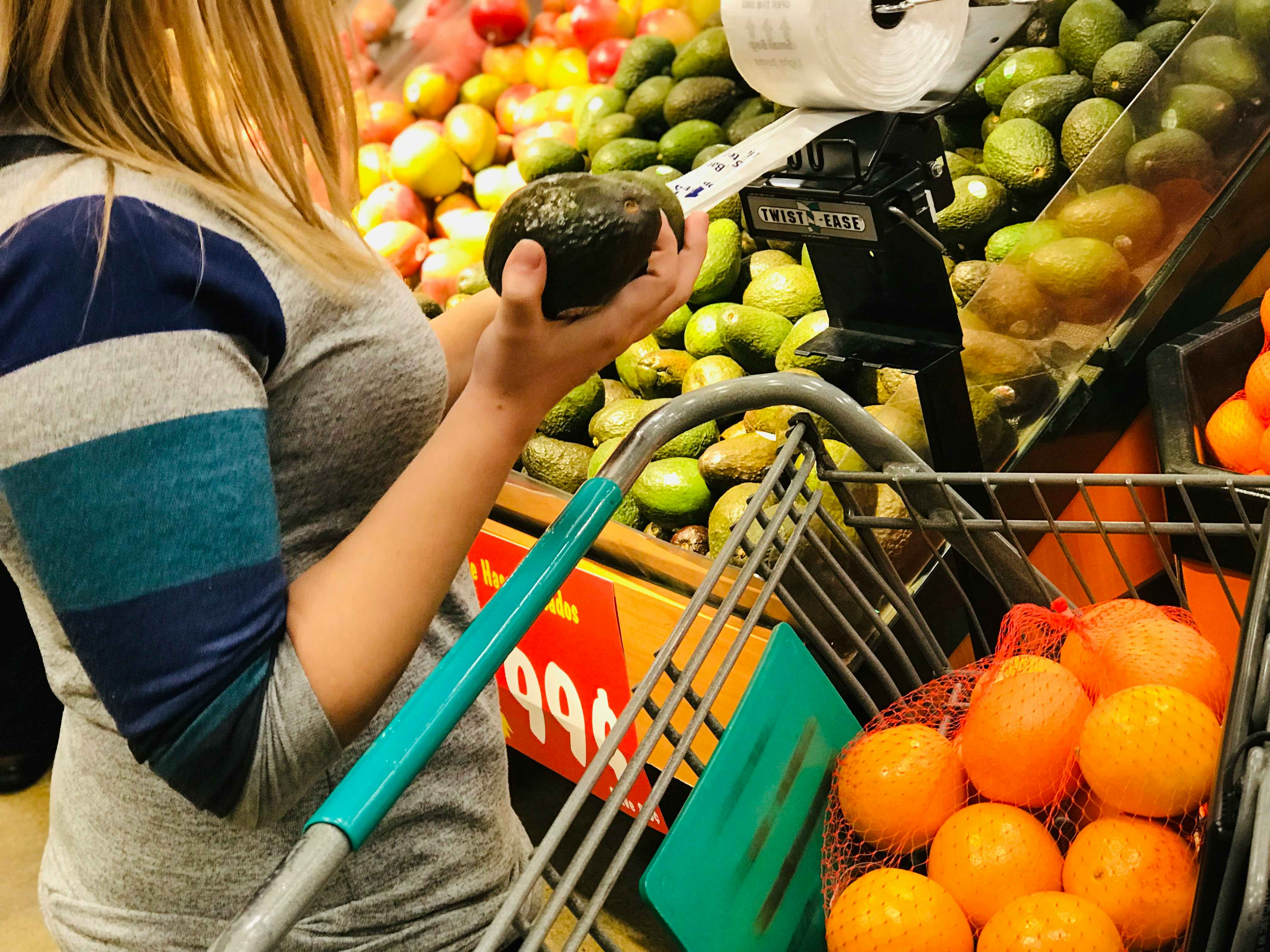 Woman about to bag an avocado in the produce aisle of a grocery store.