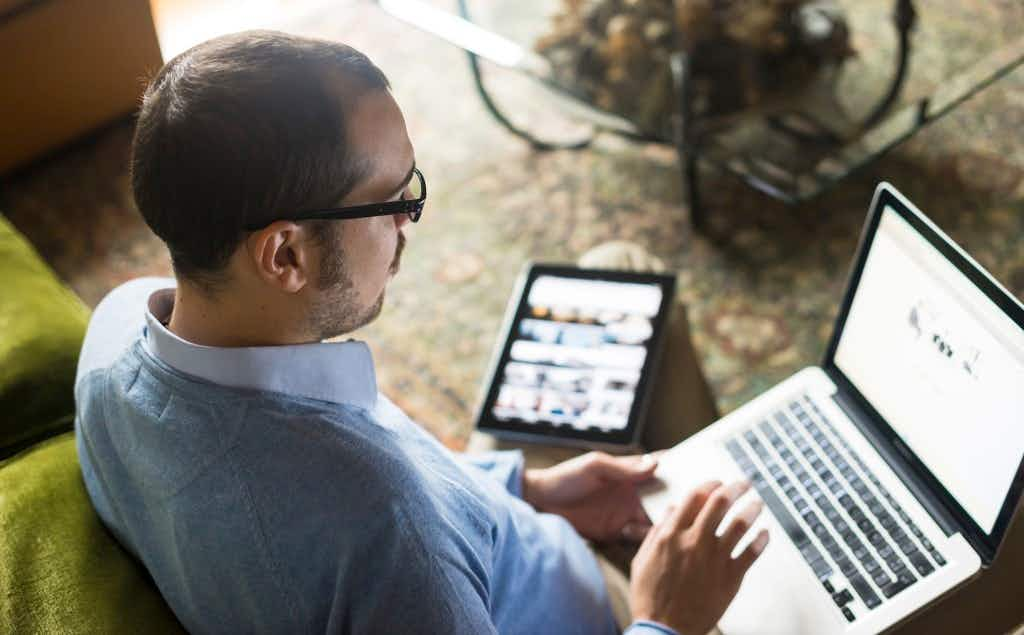 man on laptop with tablet nearby