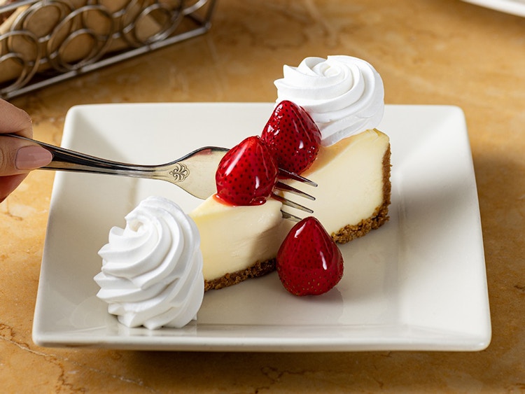 a person cutting into a slide of cheesecake from the cheesecake factory