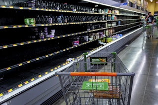 A Walmart shopping cart in front of empty shelves inside Walmart