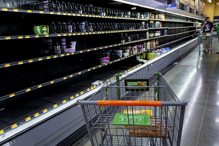 A Walmart shopping cart in front of empty shelves inside Walmart