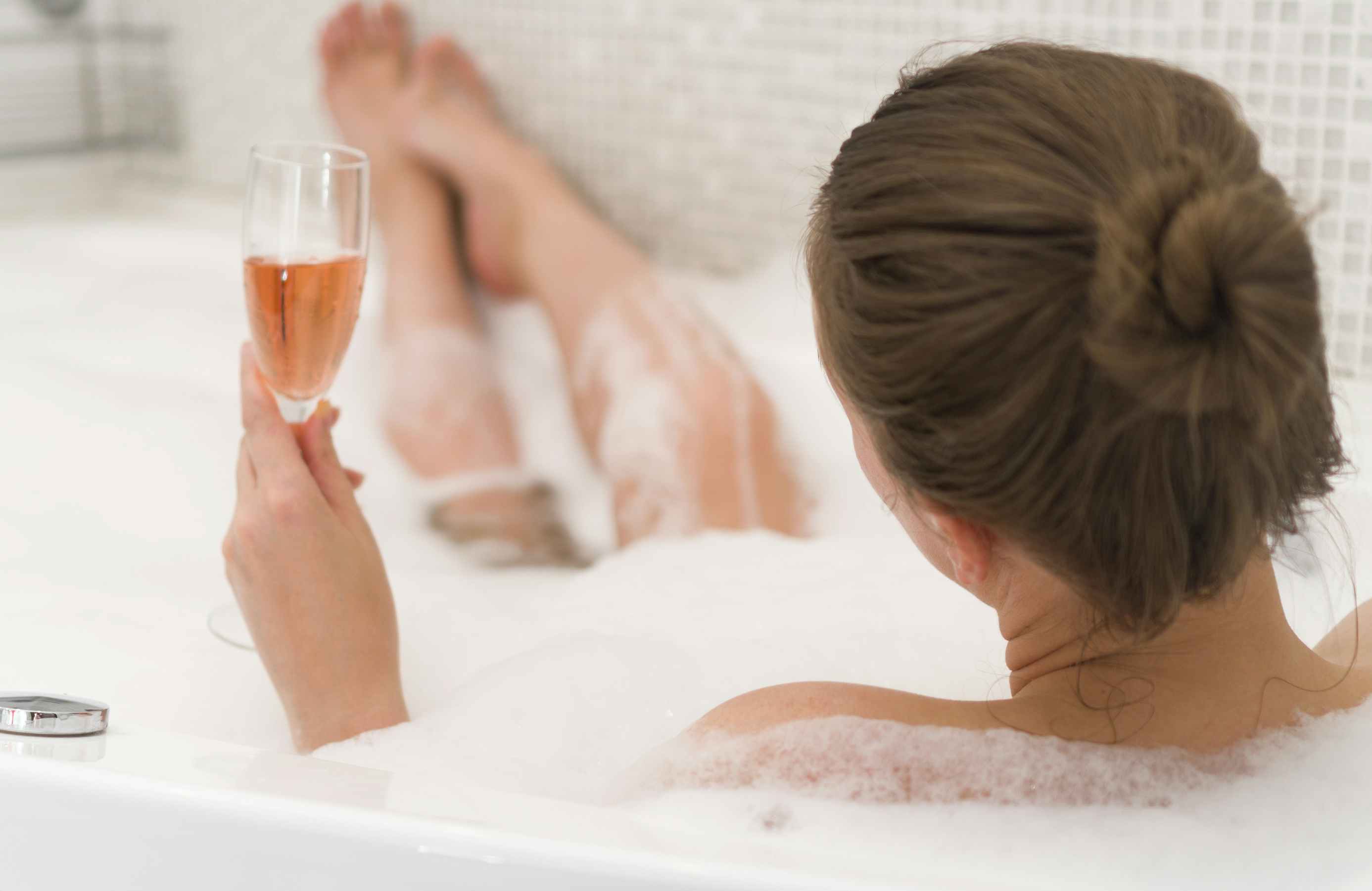 A person in a bubble bath holding a glass of champagne