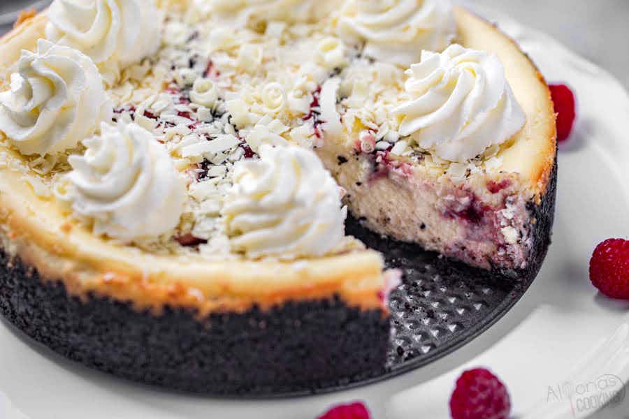 A close up of a white chocolate raspberry cheesecake with a slice taken out.