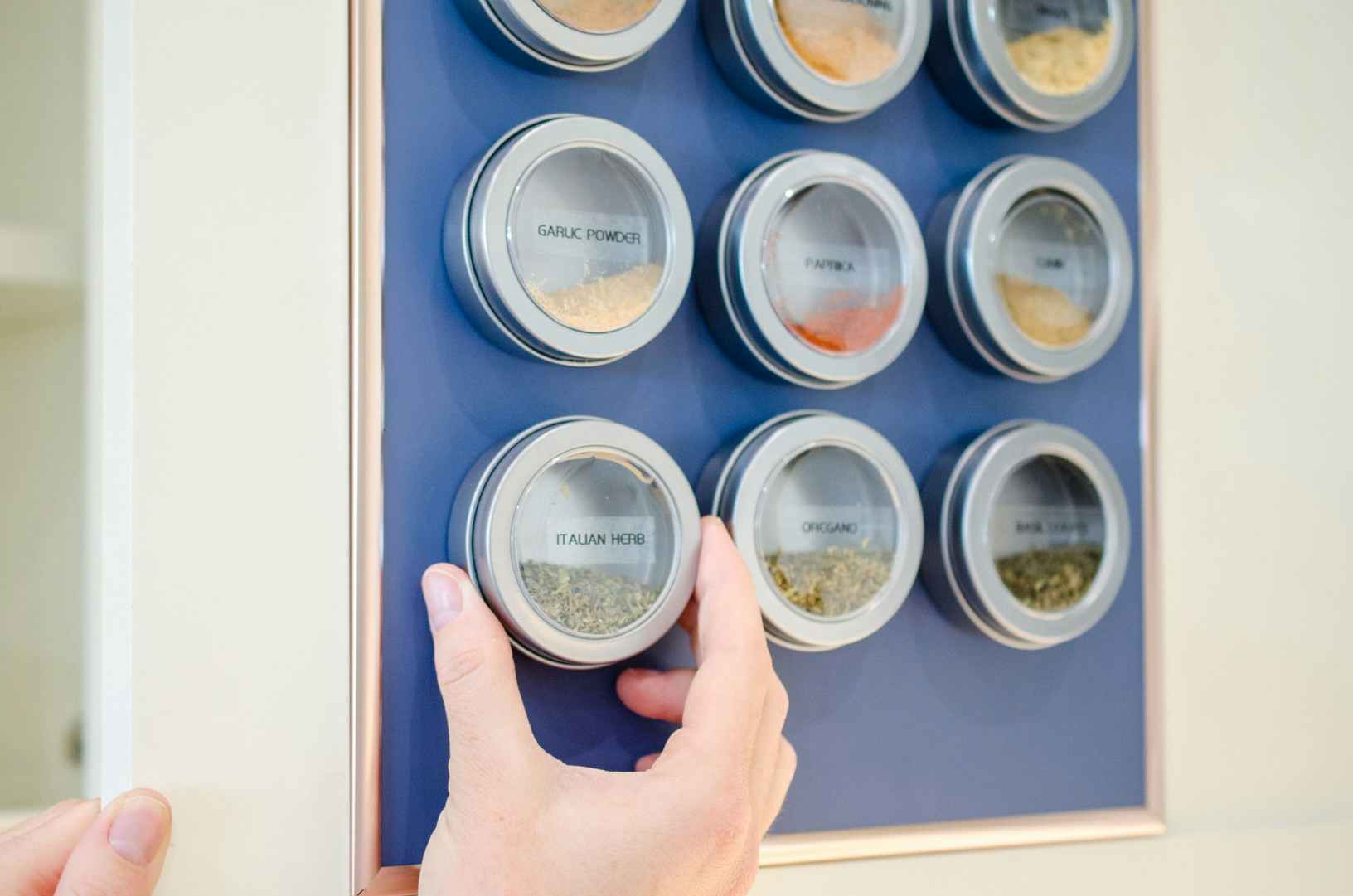 a person putting up a magnetic spice container on a magnetic board in a cabinet door 