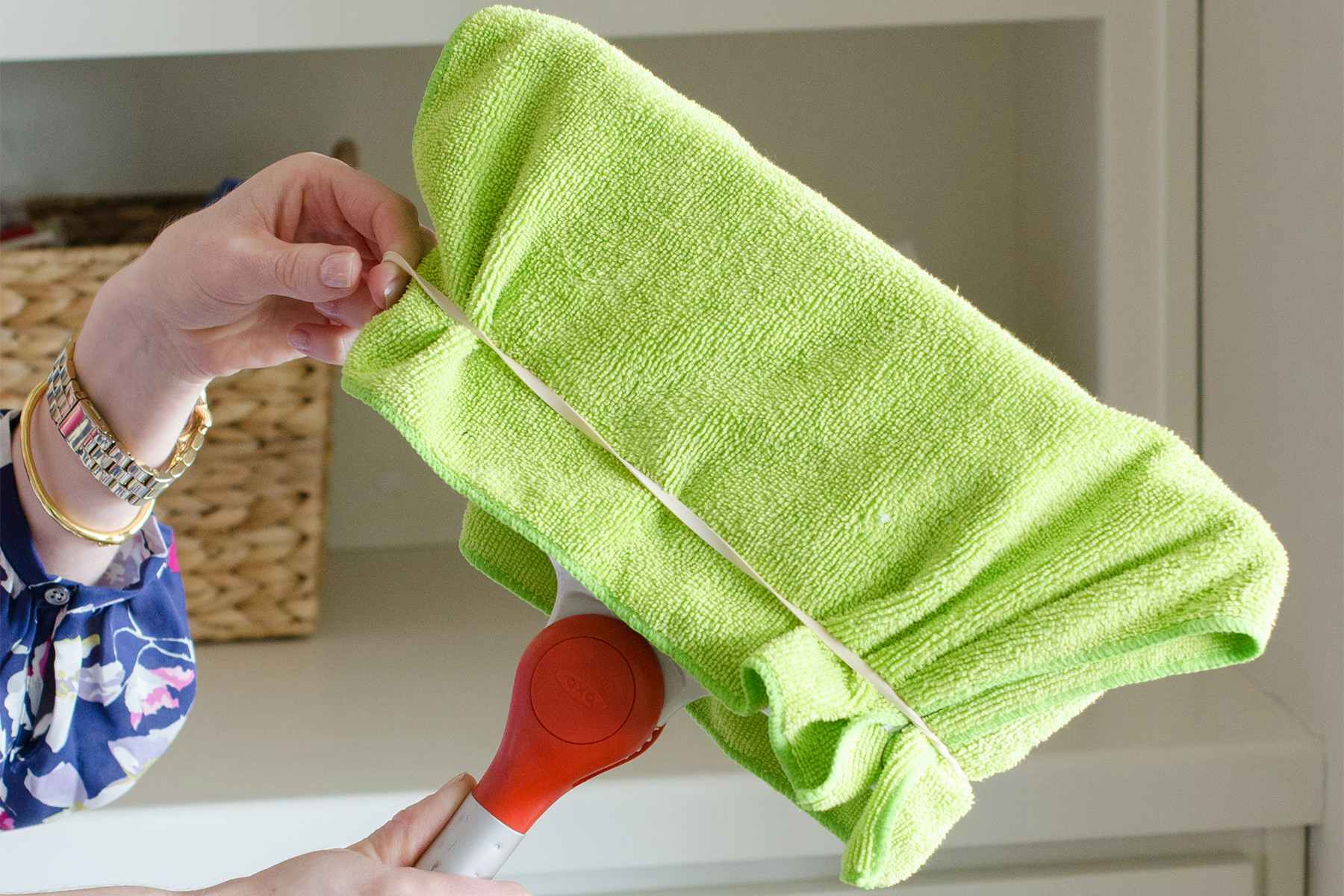 someone using a rubber band to secure a microfiber cloth over a broom.