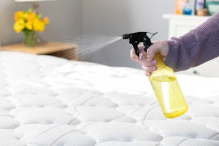 A person spraying the contents of a yellow spray bottle onto a mattress