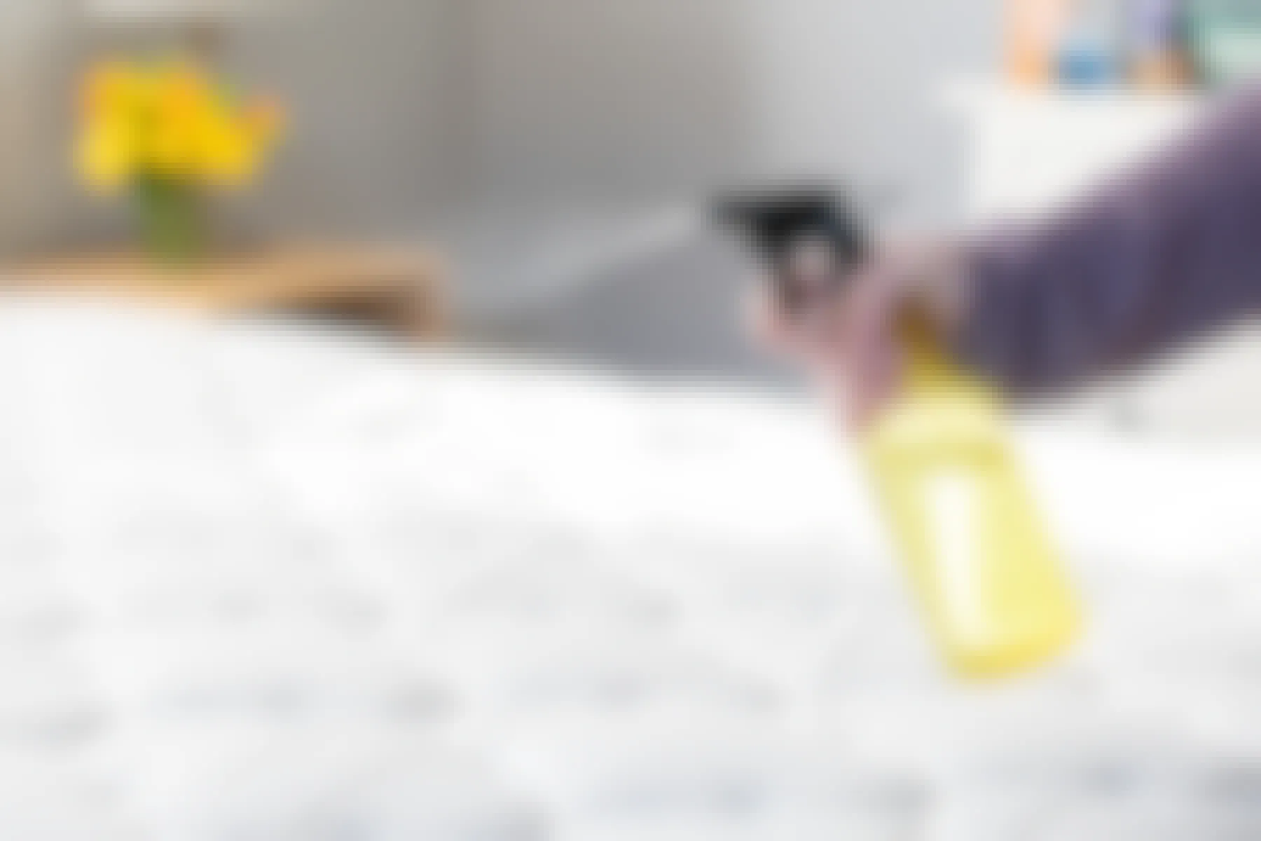 A person spraying the contents of a yellow spray bottle onto a mattress 