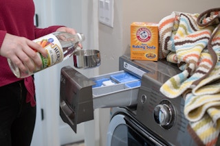 someone pouring vinegar into measuring cup next to washing machine and baking soda