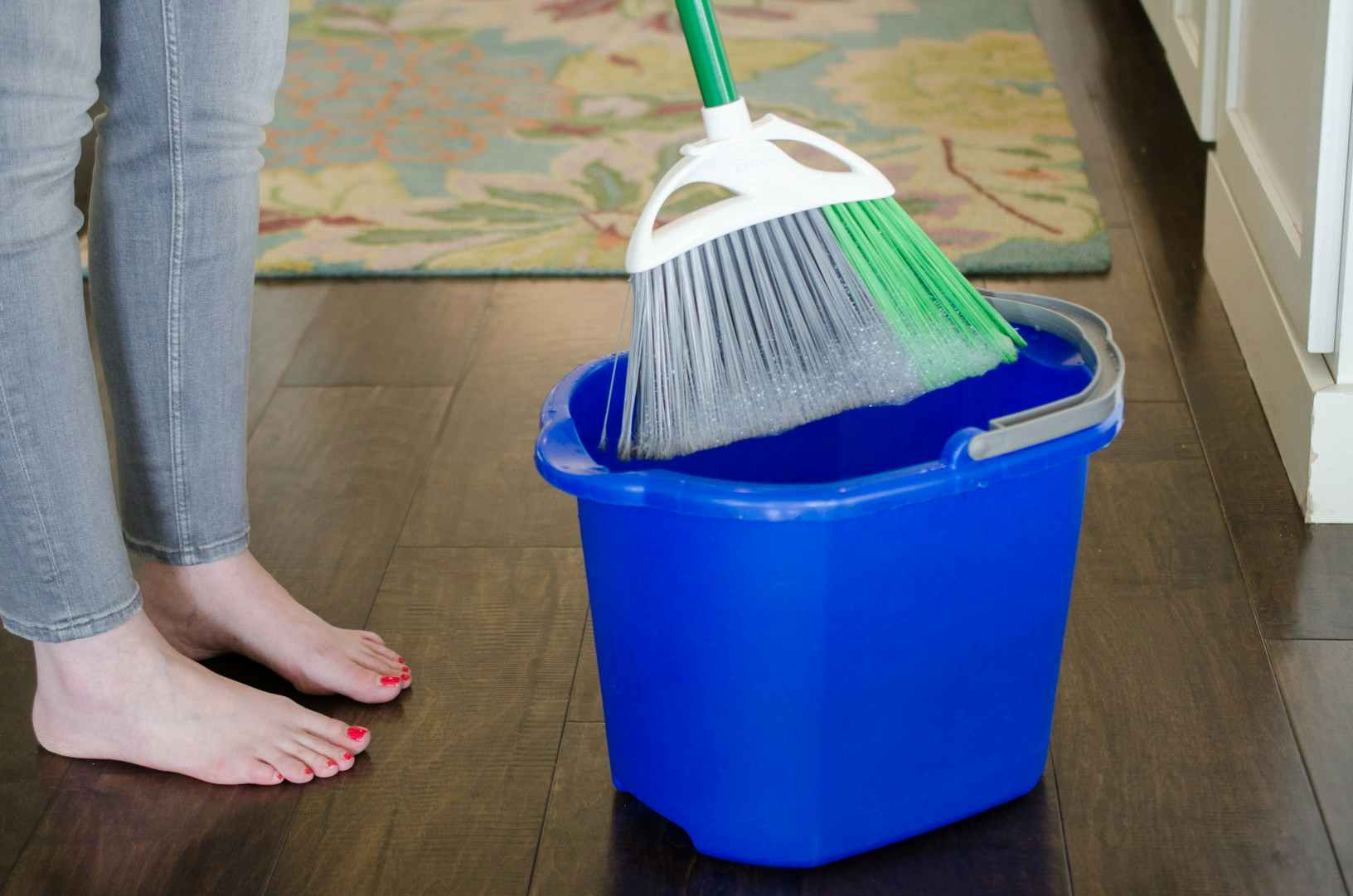 a woman cleaning her home and dunking her broom in a deep cleaning solution