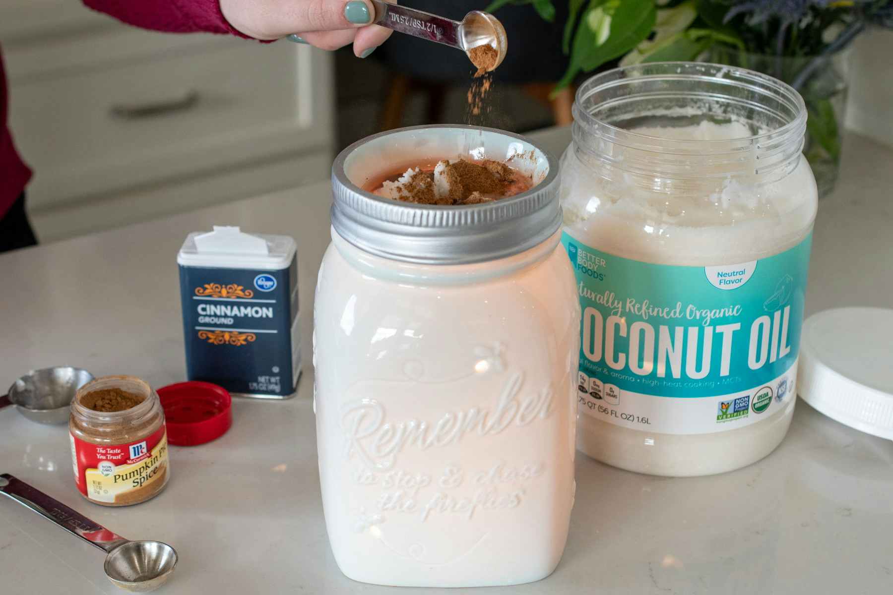 Someone adding a teaspoon of cinnamon to a candle warmer with coconut oil nearby