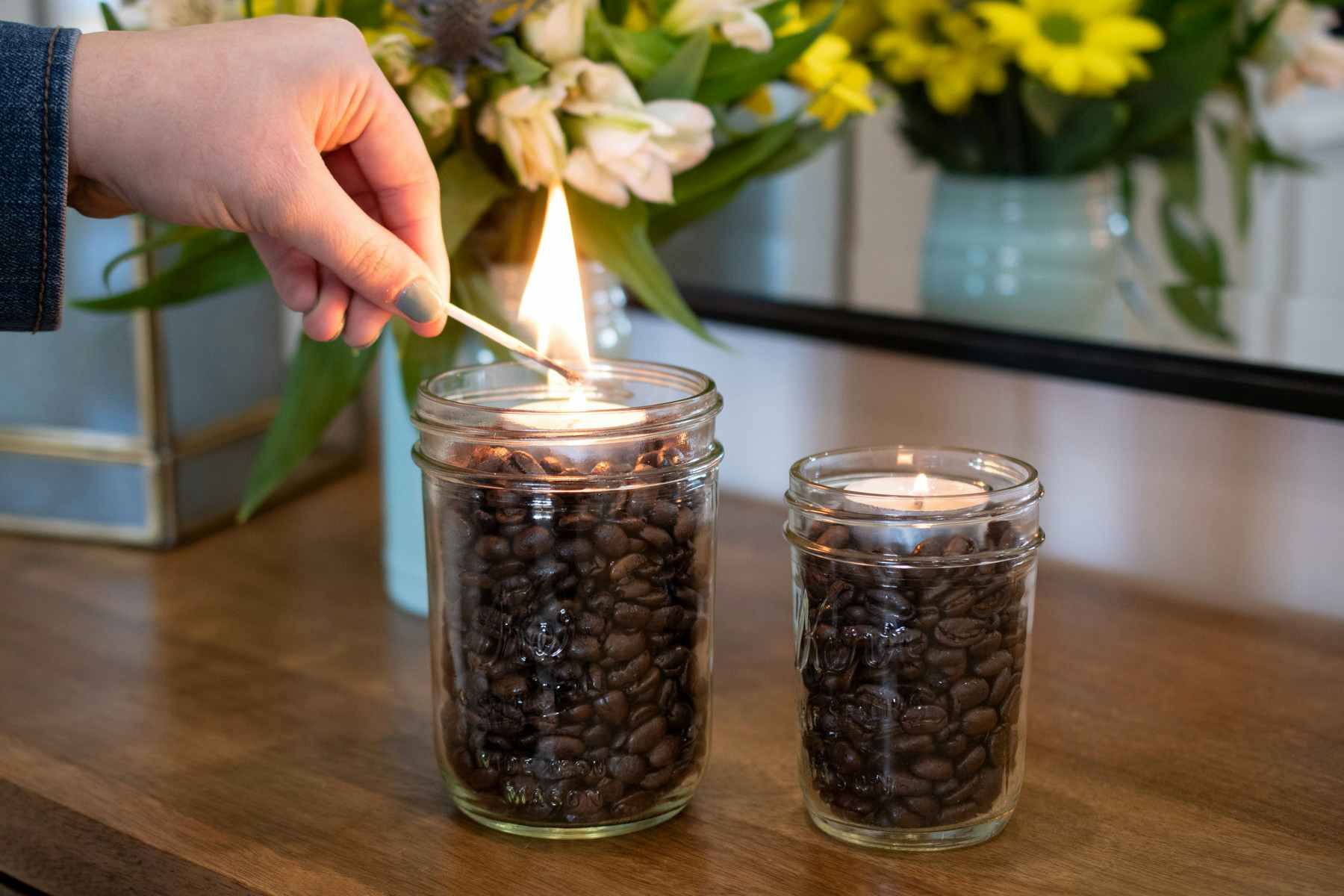 Woman lighting a tealight placed in a jar filled with coffee beans