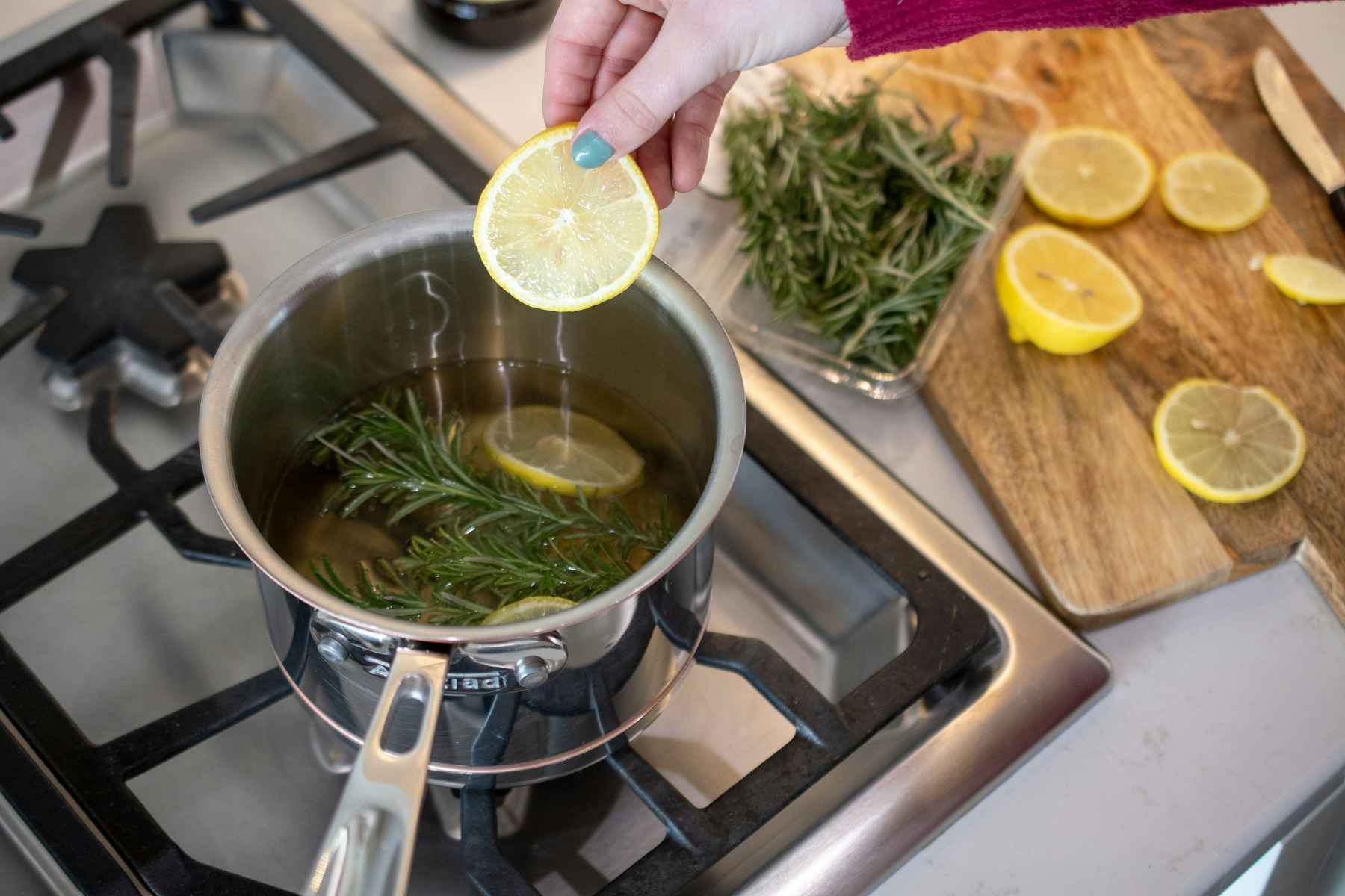 Woman placing a lemon slice into a pot with water and rosemary sprigs