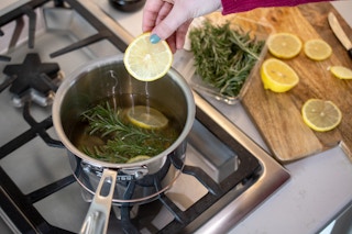 Woman placing a lemon slice into a pot with water and rosemary sprigs