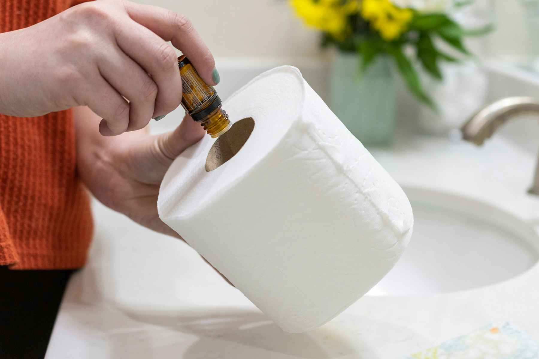 A woman adding drops of essential oil to the tube of a toilet paper roll