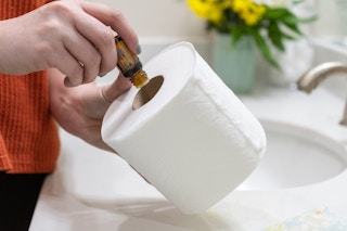 A woman adding drops of essential oil to the tube of a toilet paper roll