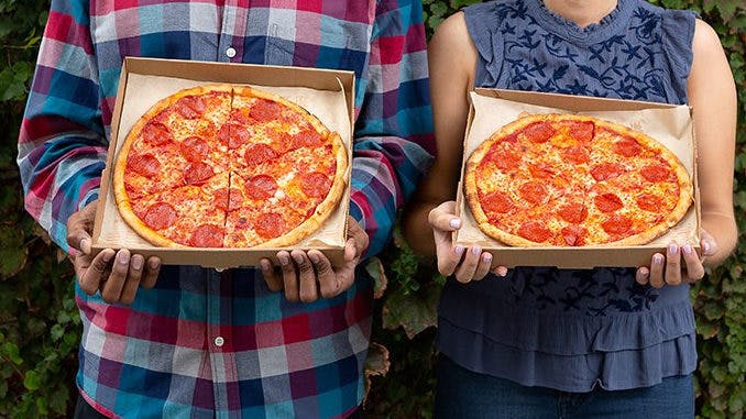 Two people holding pepperoni pizzas