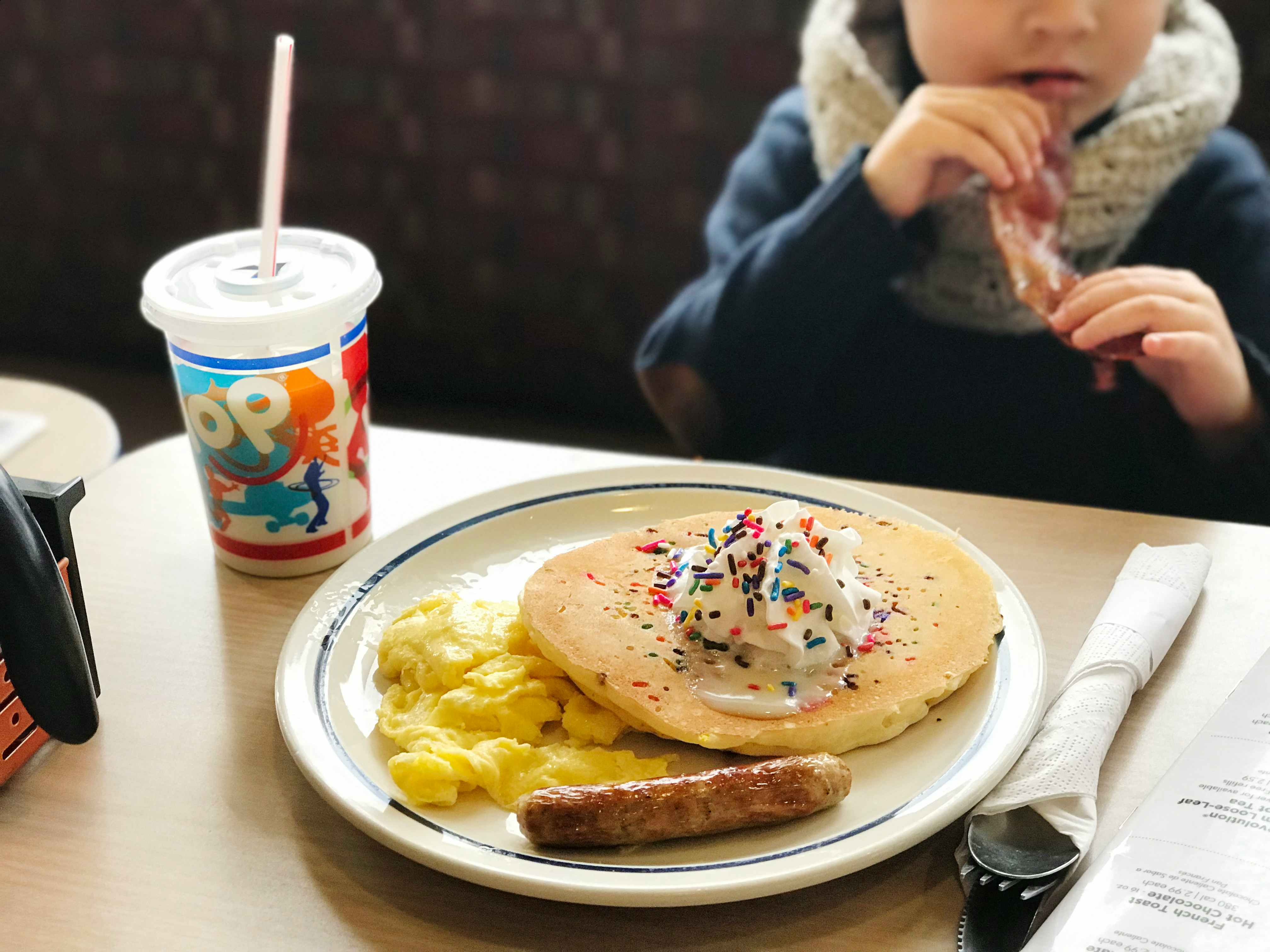 A child eating a pancake, sausage, and scrambled eggs kids meal.