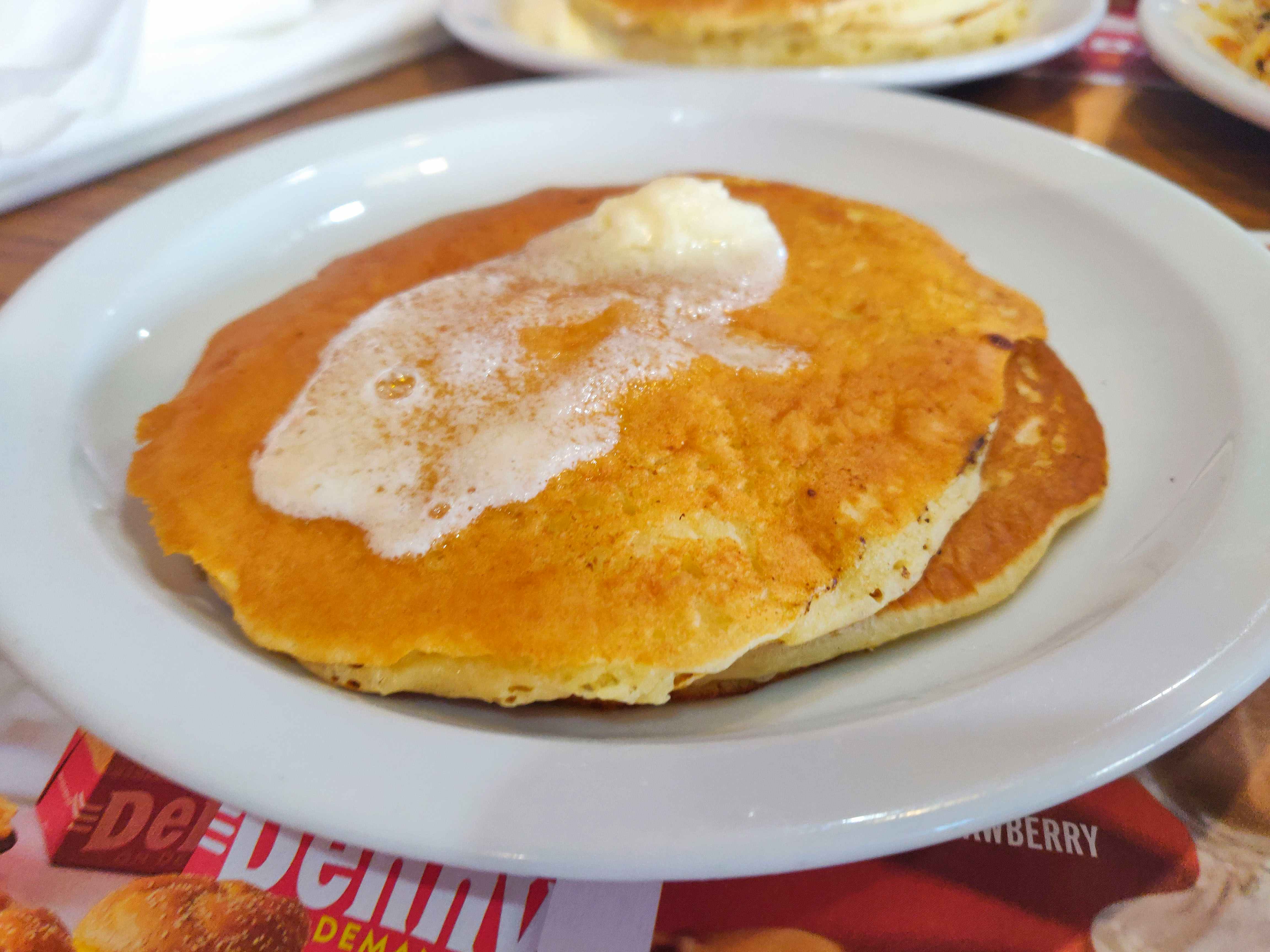 A plate of two plain pancakes with butter on top, sitting on a table at Denny's.