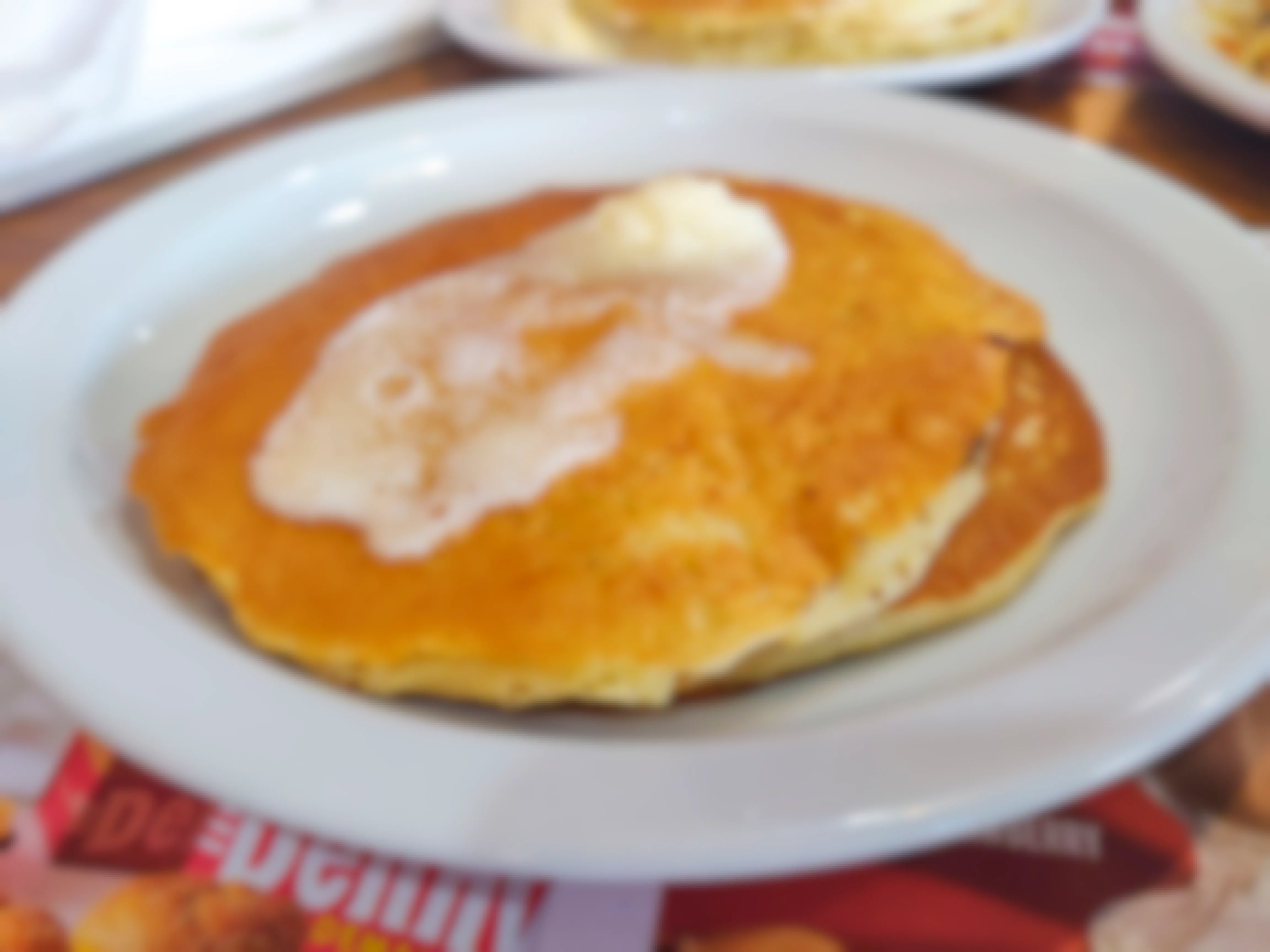 A plate of two plain pancakes with butter on top, sitting on a table at Denny's.