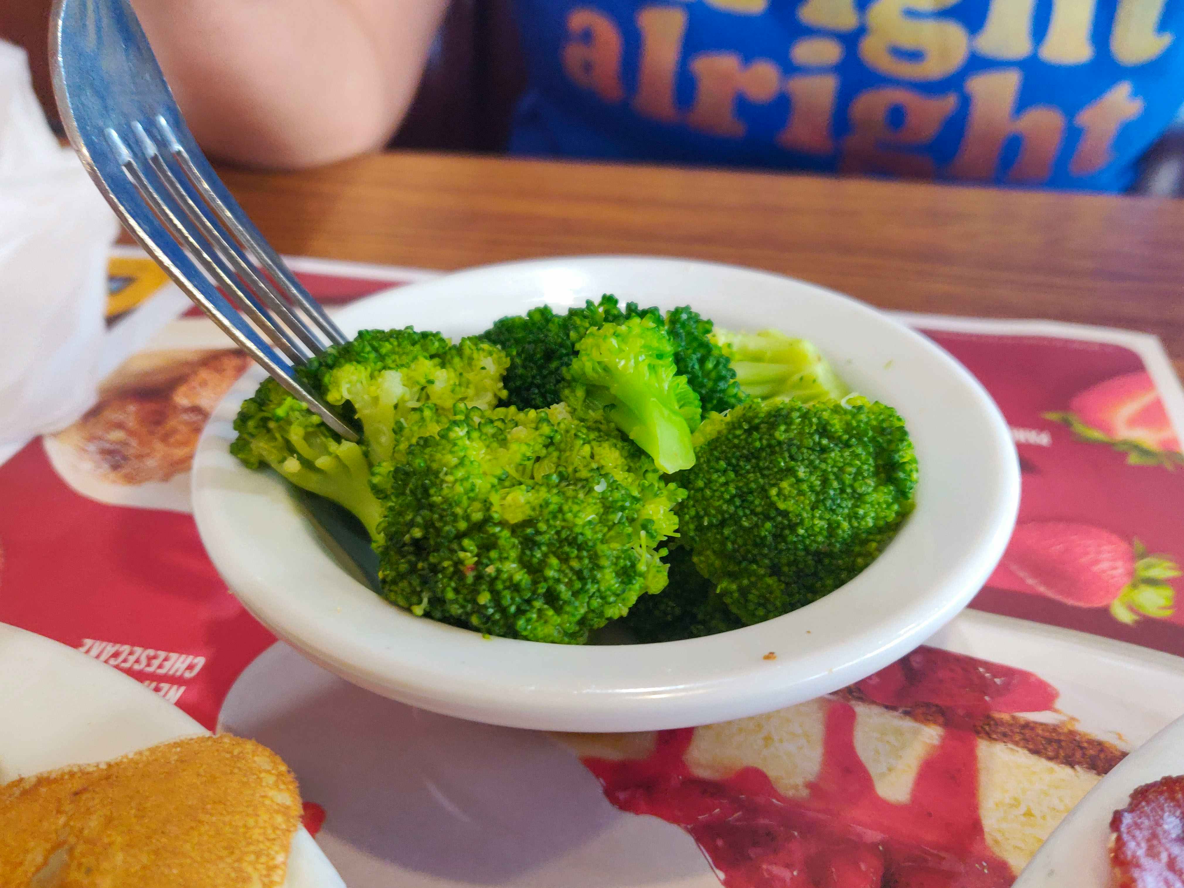 A fork sticking into a small bowl of broccoli sitting on the table at Denny's.
